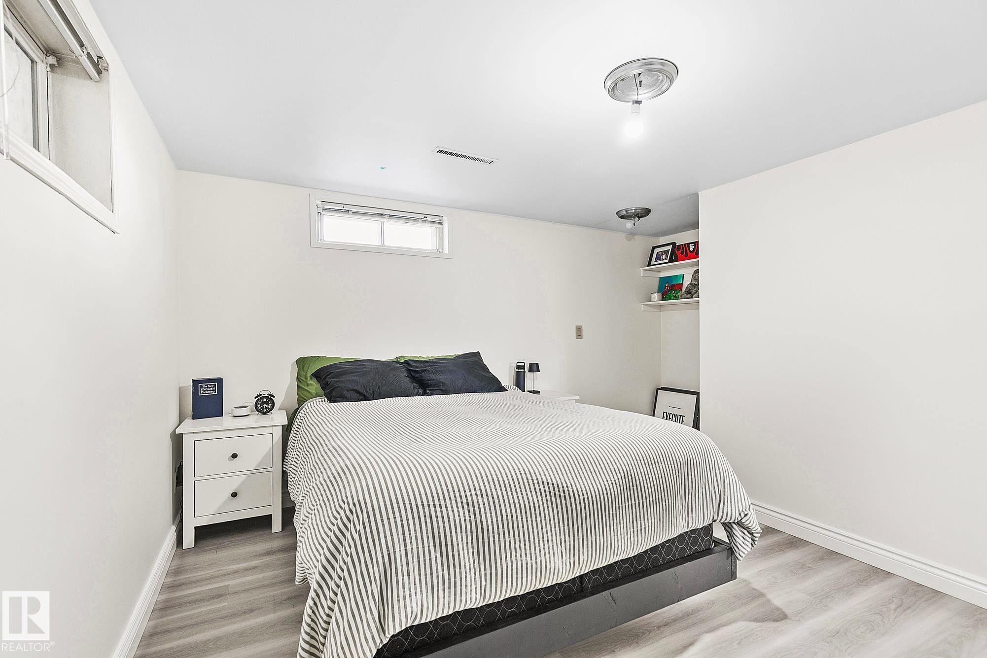 Bedroom featuring light wood-finish flooring, white painted walls, and two visible egress windows - 17059 98 Street, Edmonton, AB - Indoor Photo Showing Bedroom