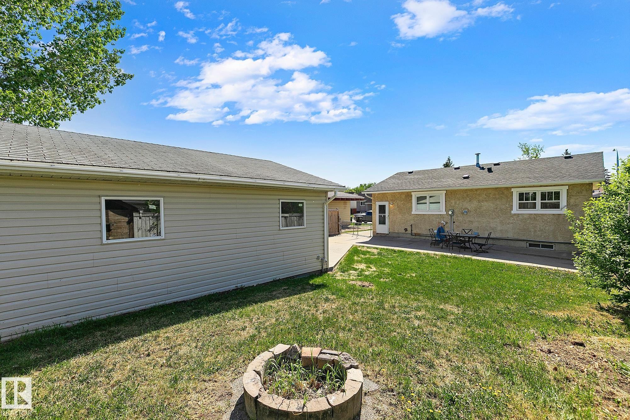 Expansive backyard featuring a stone-lined fire pit, a detached garage with horizontal siding, and a concrete patio - 17059 98 Street, Edmonton, AB - Outdoor