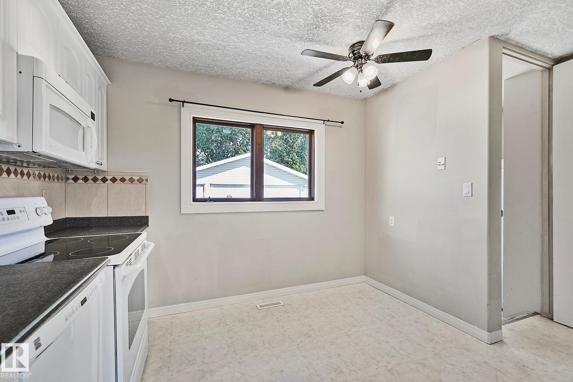 Kitchen dining area featuring white cabinetry, dark countertops, a built-in microwave, tile backsplash, and a ceiling fan with light fixture - 17059 98 Street, Edmonton, AB - Indoor Photo Showing Kitchen