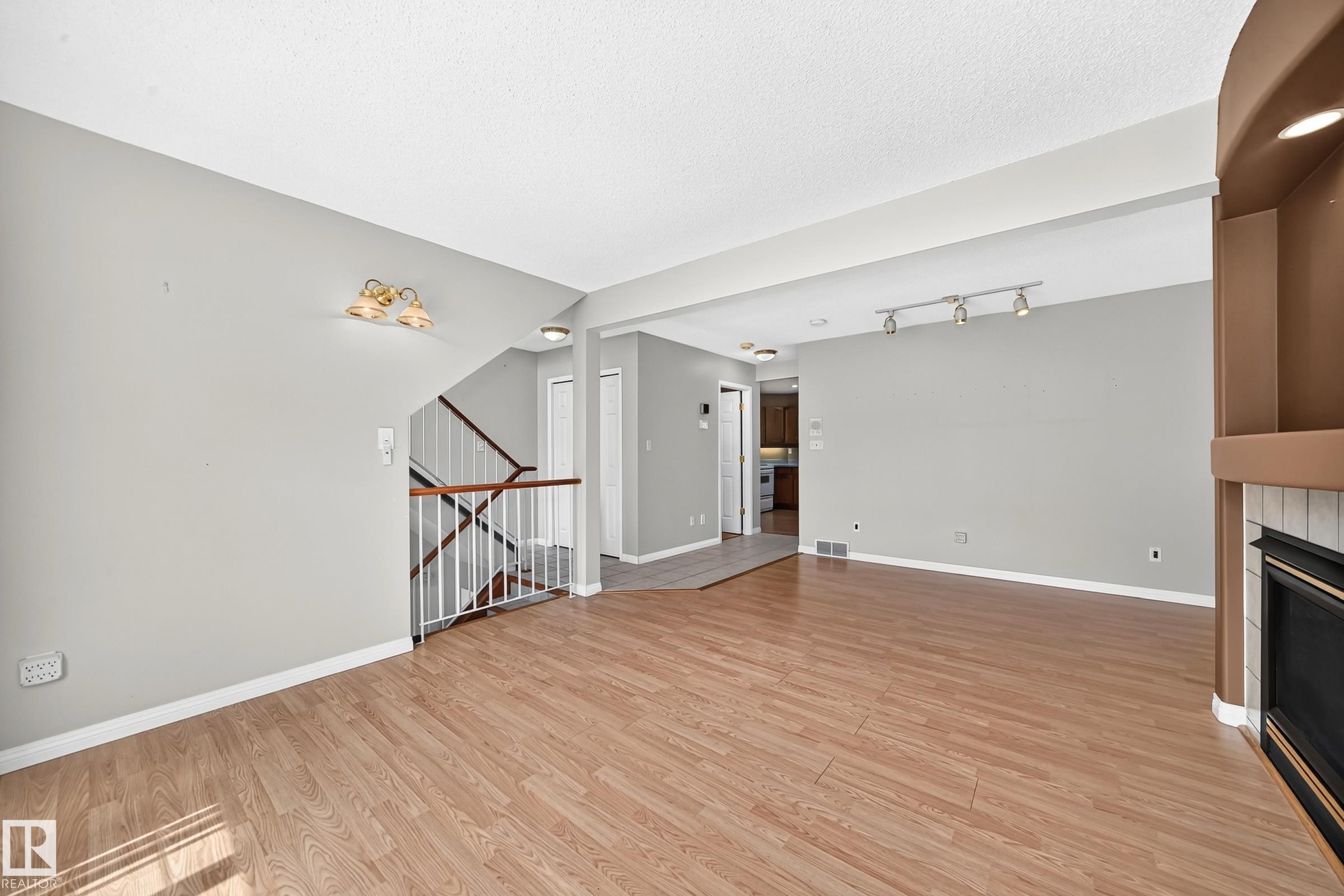 Spacious living area featuring wood-finish flooring, a white-tiled fireplace with hearth, and a built-in shelving unit - #51 9630 176 St Nw, Edmonton, AB - Indoor With Fireplace