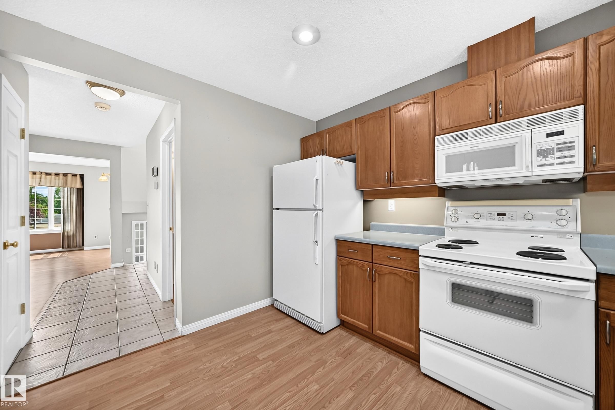 Kitchen featuring wood-finish flooring, wood cabinetry, white appliances, and light-toned countertops - #51 9630 176 St Nw, Edmonton, AB - Indoor Photo Showing Kitchen