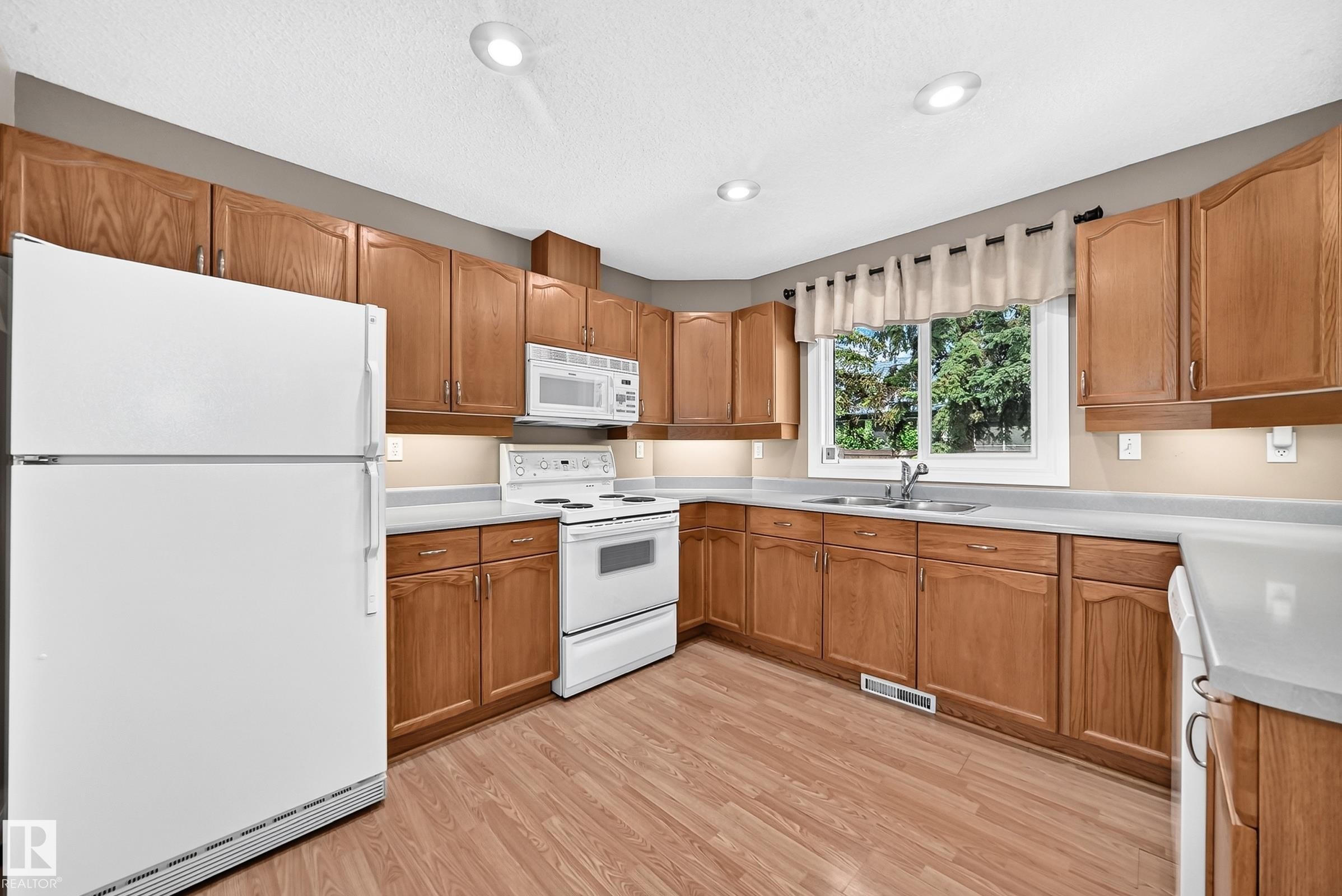 Kitchen featuring wood-finish cabinetry, light-toned countertops, and wood-finish flooring - #51 9630 176 St Nw, Edmonton, AB - Indoor Photo Showing Kitchen With Double Sink