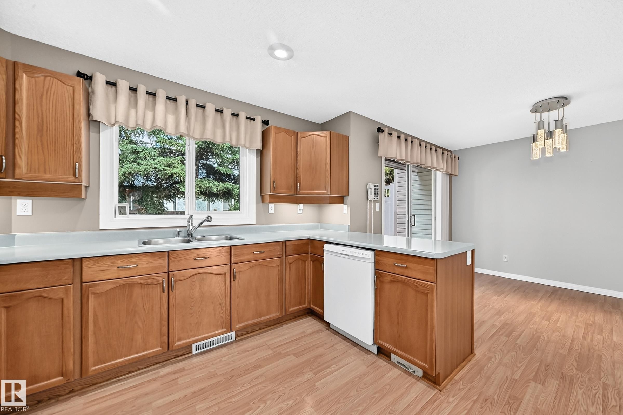 Kitchen featuring wood-finish flooring, a double basin stainless steel sink, light countertops, and wood cabinetry - #51 9630 176 St Nw, Edmonton, AB - Indoor Photo Showing Kitchen With Double Sink