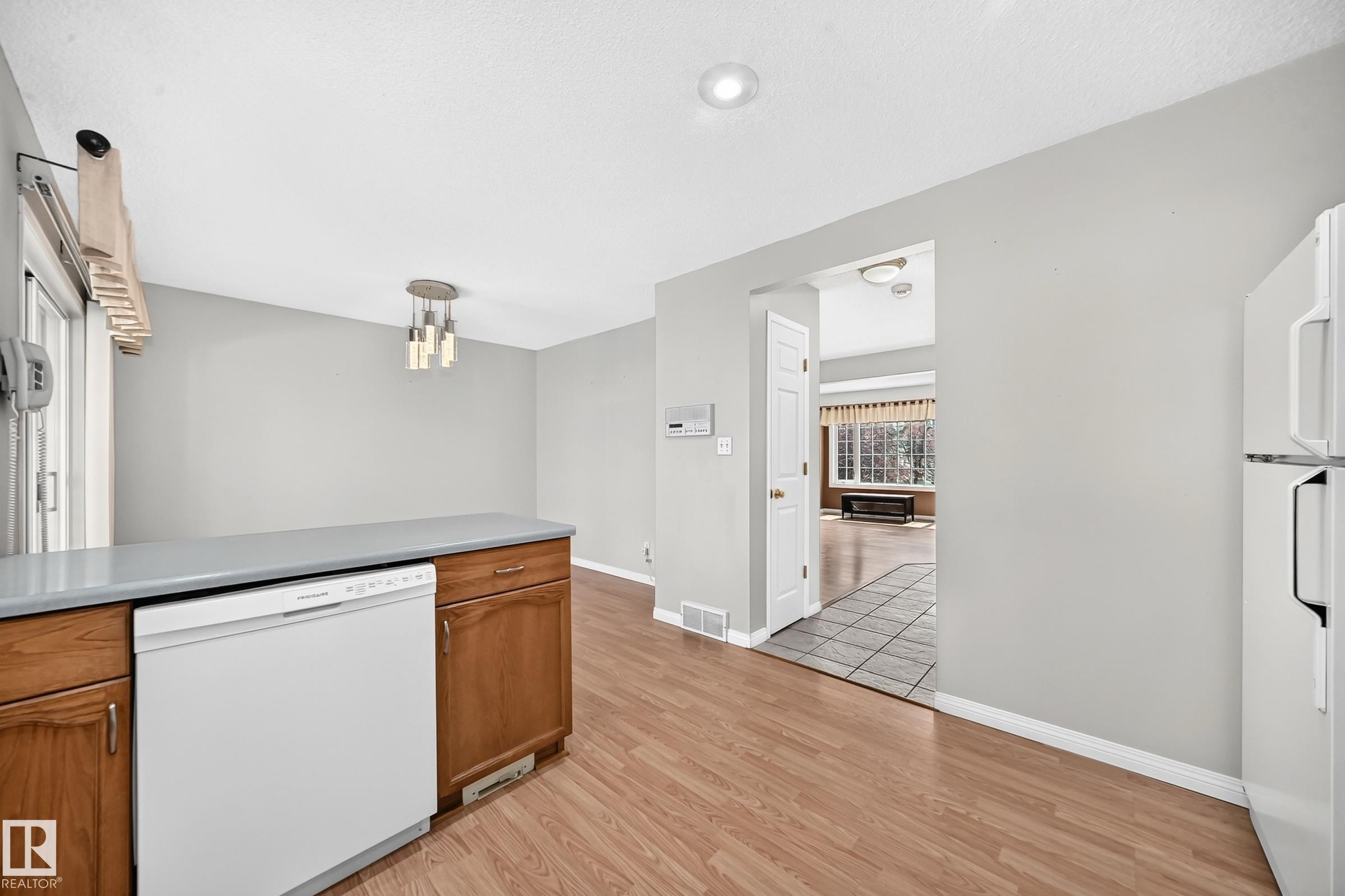 Kitchen area featuring wood-finish flooring, white built-in dishwasher, light gray countertops, and wood cabinetry - #51 9630 176 St Nw, Edmonton, AB - Indoor Photo Showing Kitchen