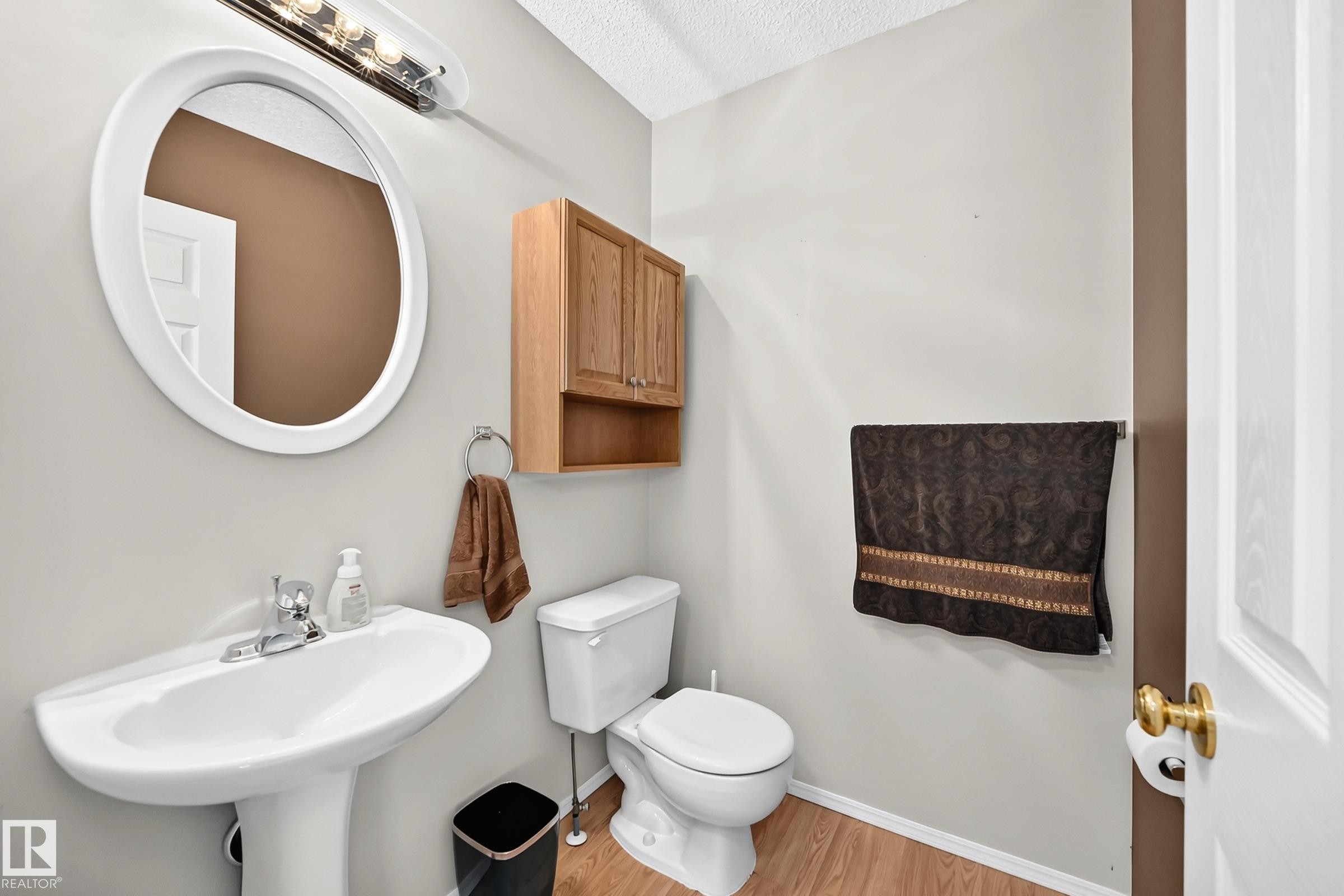 Pedestal sink with chrome faucet, oval mirror, and overhead vanity lighting - #51 9630 176 St Nw, Edmonton, AB - Indoor Photo Showing Bathroom