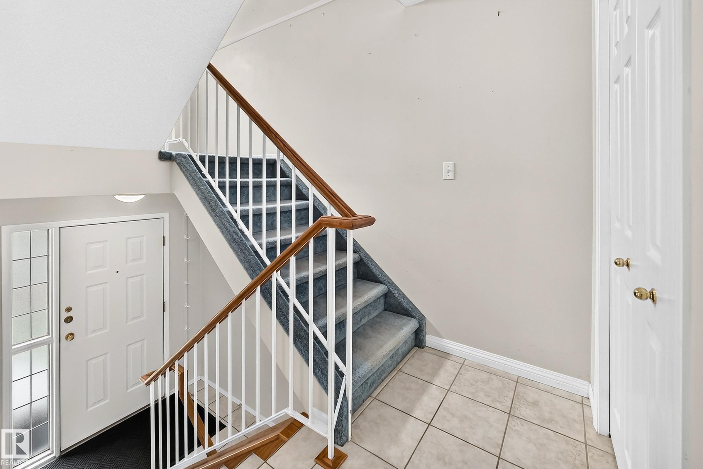 Foyer featuring a white paneled entry door with sidelight, tile flooring, and carpeted stairs with white balusters and wood handrails - #51 9630 176 St Nw, Edmonton, AB - Indoor Photo Showing Other Room