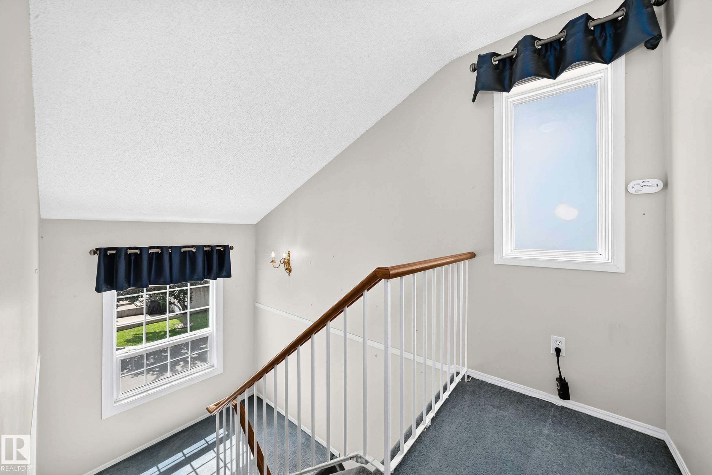 Staircase featuring a wood handrail, white balusters, and a textured carpeted runner - #51 9630 176 St Nw, Edmonton, AB - Indoor Photo Showing Other Room