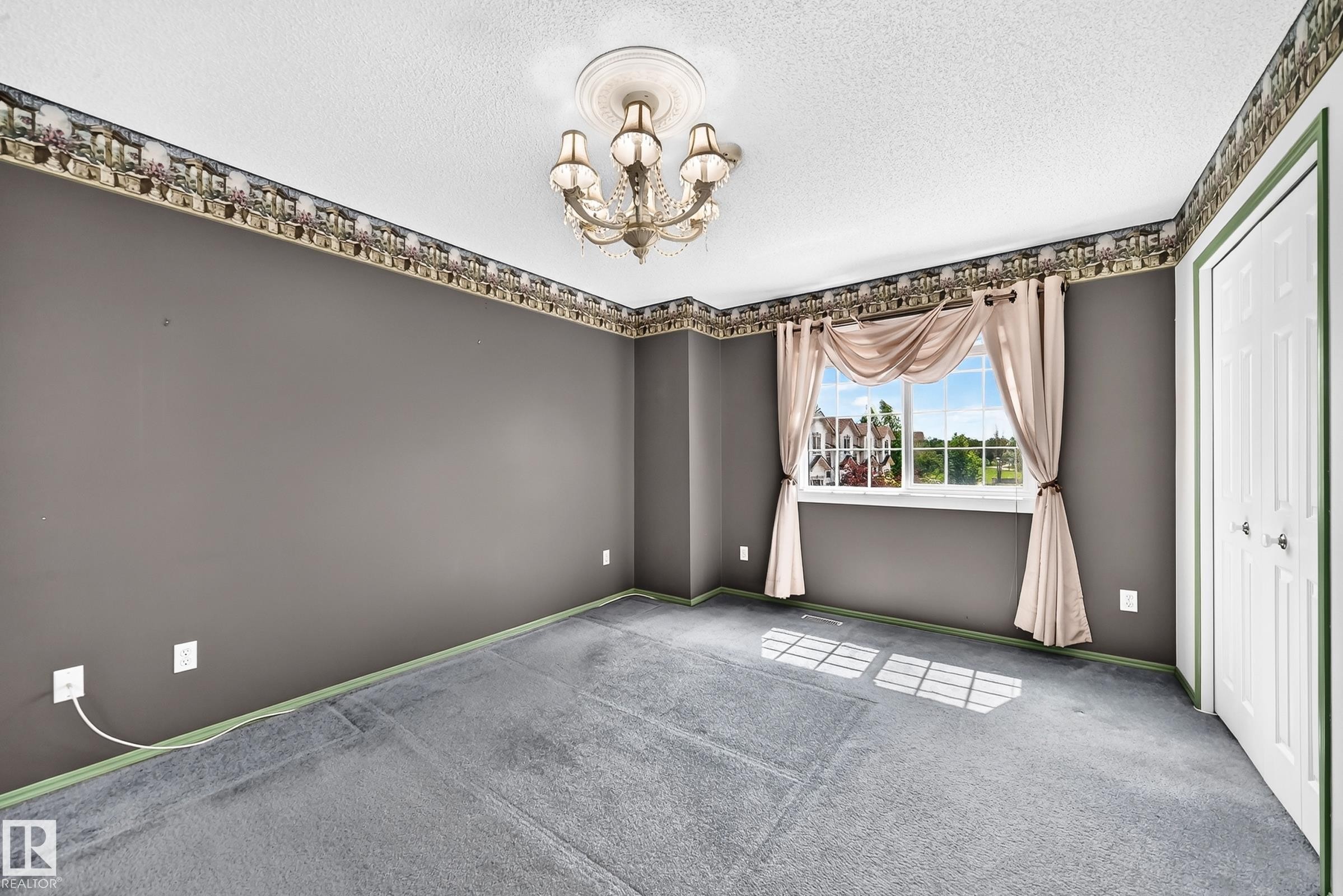 Spacious room featuring a central chandelier with decorative ceiling medallion, neutral gray walls, and light blue carpeting - #51 9630 176 St Nw, Edmonton, AB - Indoor