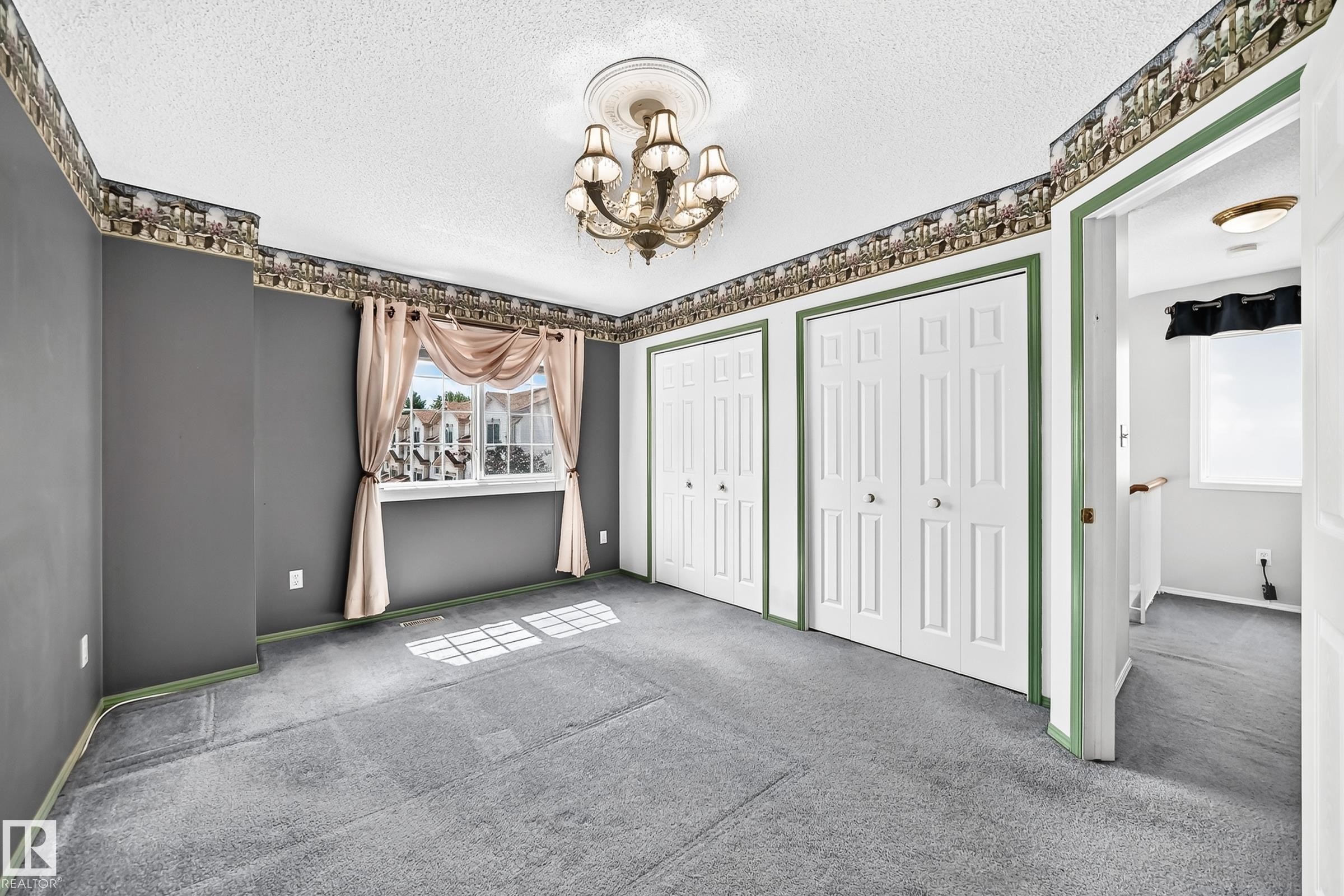 Spacious room featuring two bi-fold closet doors, a detailed ceiling medallion with a chandelier, and a large window with exterior views - #51 9630 176 St Nw, Edmonton, AB - Indoor Photo Showing Other Room
