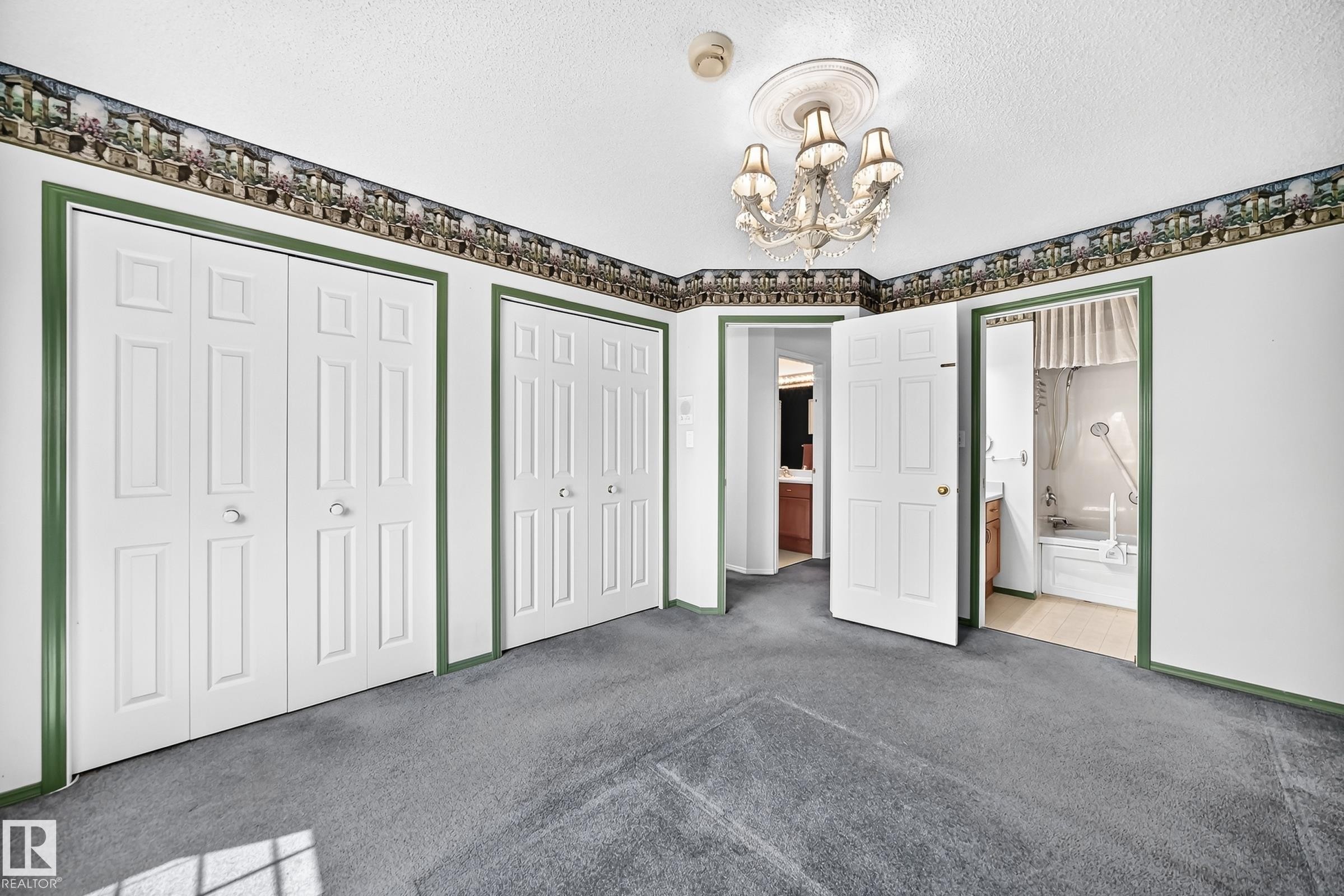 Room featuring gray carpeting, multiple bi-fold closet doors, and a decorative chandelier - #51 9630 176 St Nw, Edmonton, AB - Indoor Photo Showing Other Room