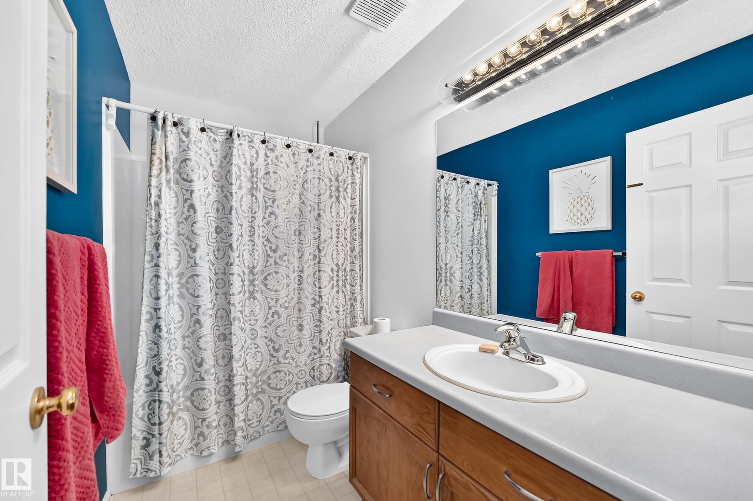 Bathroom featuring a wood-finish vanity with a light-toned countertop, an integrated sink, and an expansive wall-mounted mirror - #51 9630 176 St Nw, Edmonton, AB - Indoor Photo Showing Bathroom