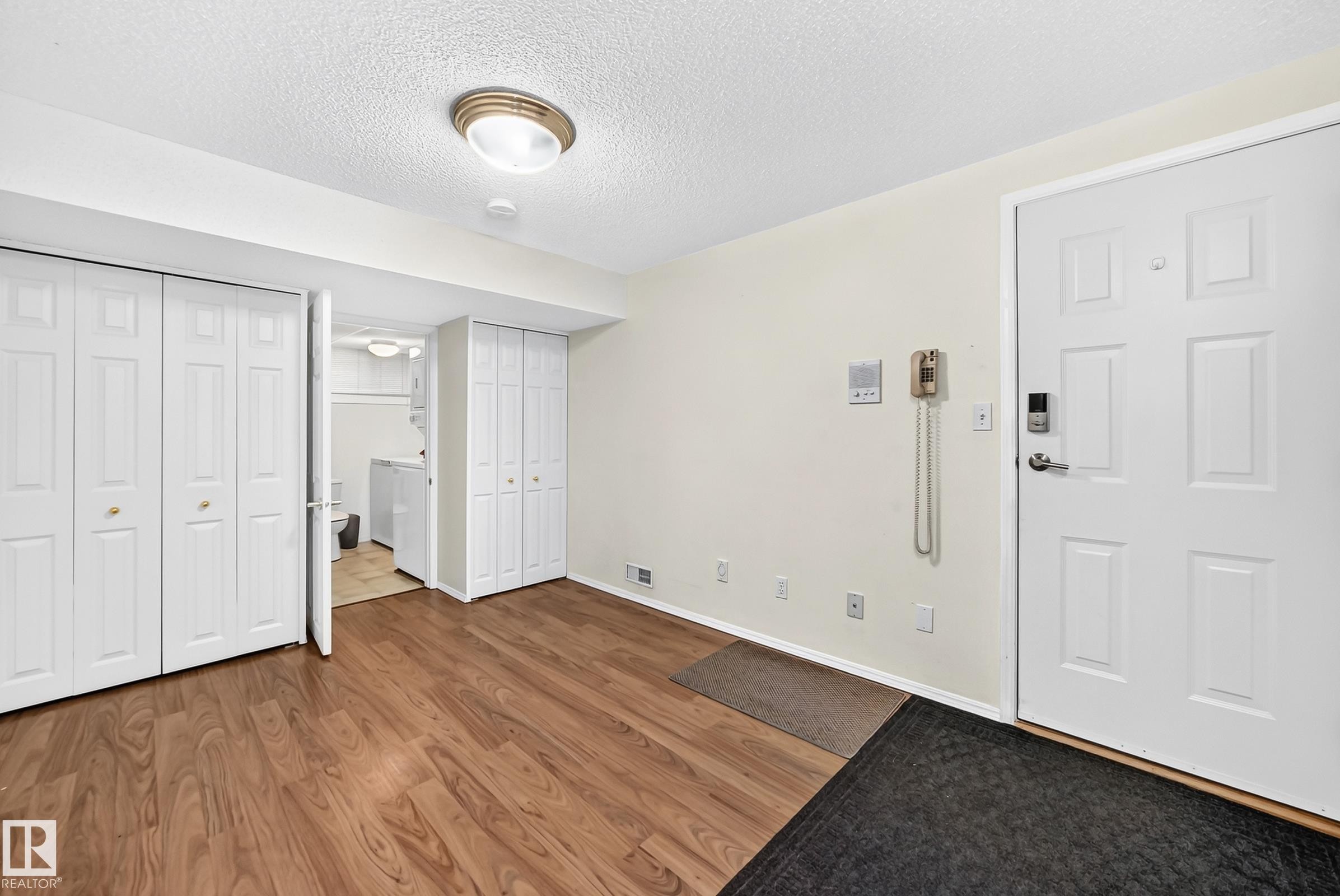 Entry area featuring wood-finish flooring, a white paneled entry door with modern hardware, and two white bi-fold closet doors - #51 9630 176 St Nw, Edmonton, AB - Indoor Photo Showing Other Room