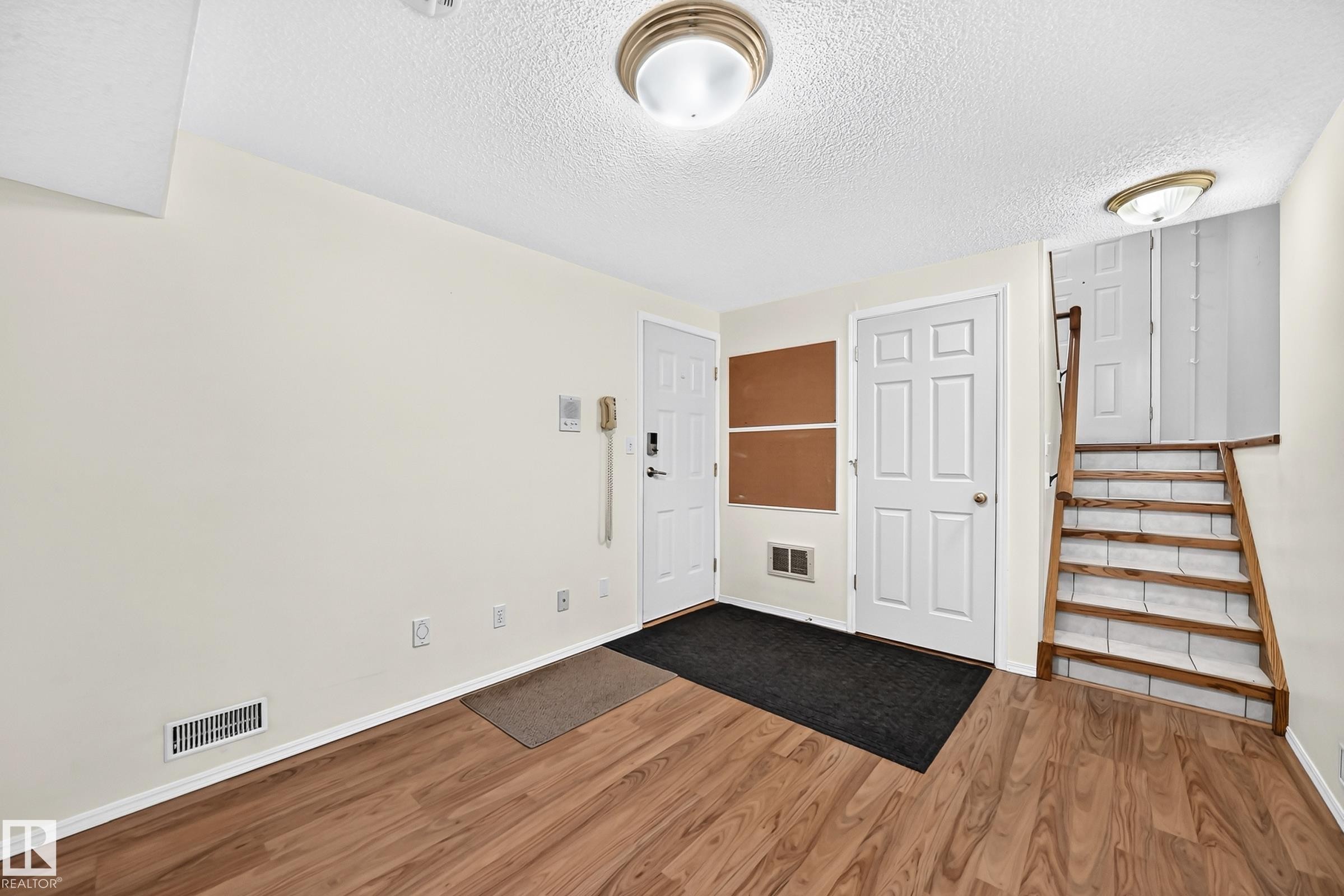Entry area featuring wood-finish flooring, white doors, and a wood staircase with white risers - #51 9630 176 St Nw, Edmonton, AB - Indoor Photo Showing Other Room