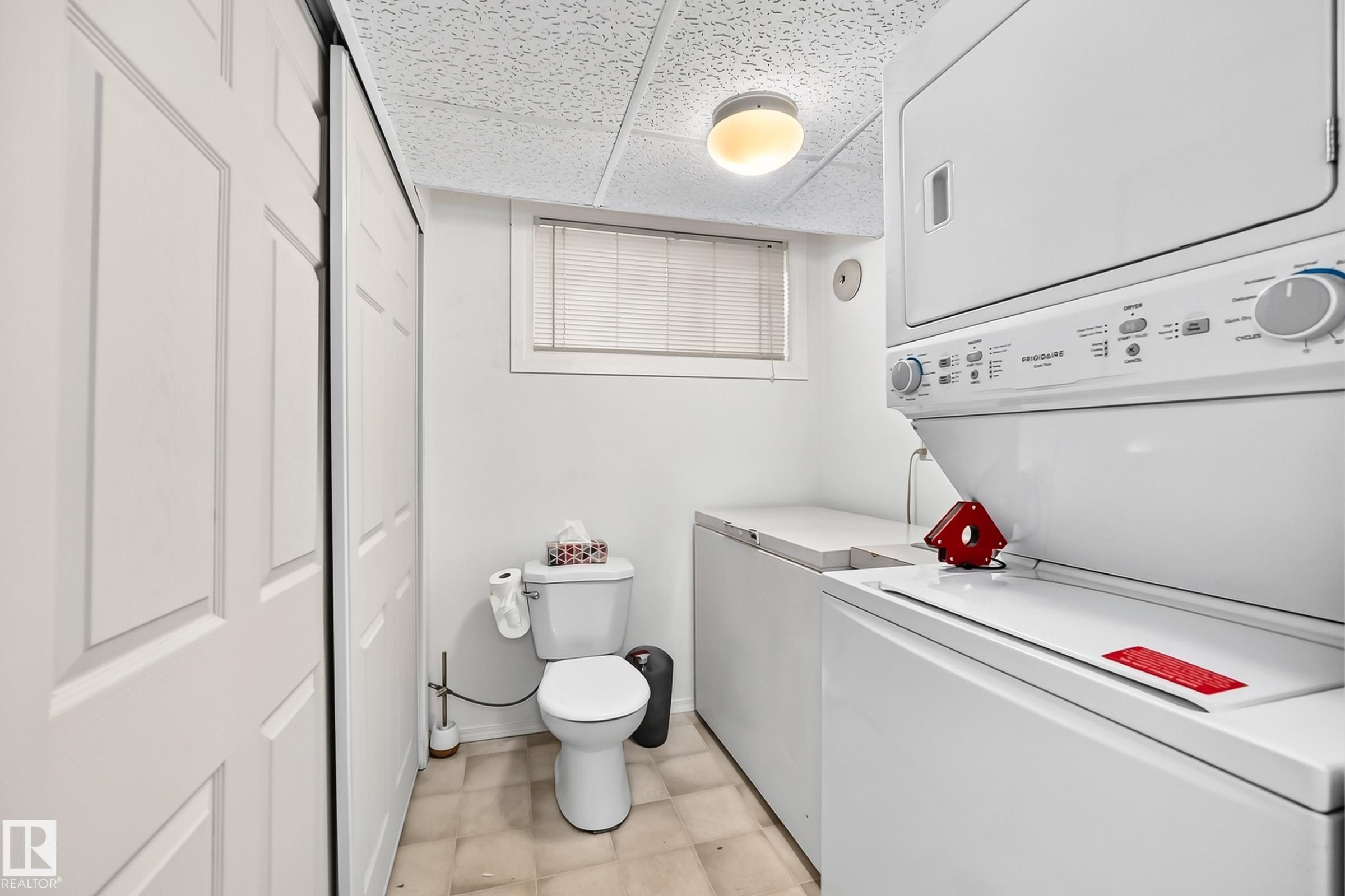Dedicated laundry area featuring a stacked washer and dryer unit, a toilet, and a window with blinds - #51 9630 176 St Nw, Edmonton, AB - Indoor Photo Showing Laundry Room