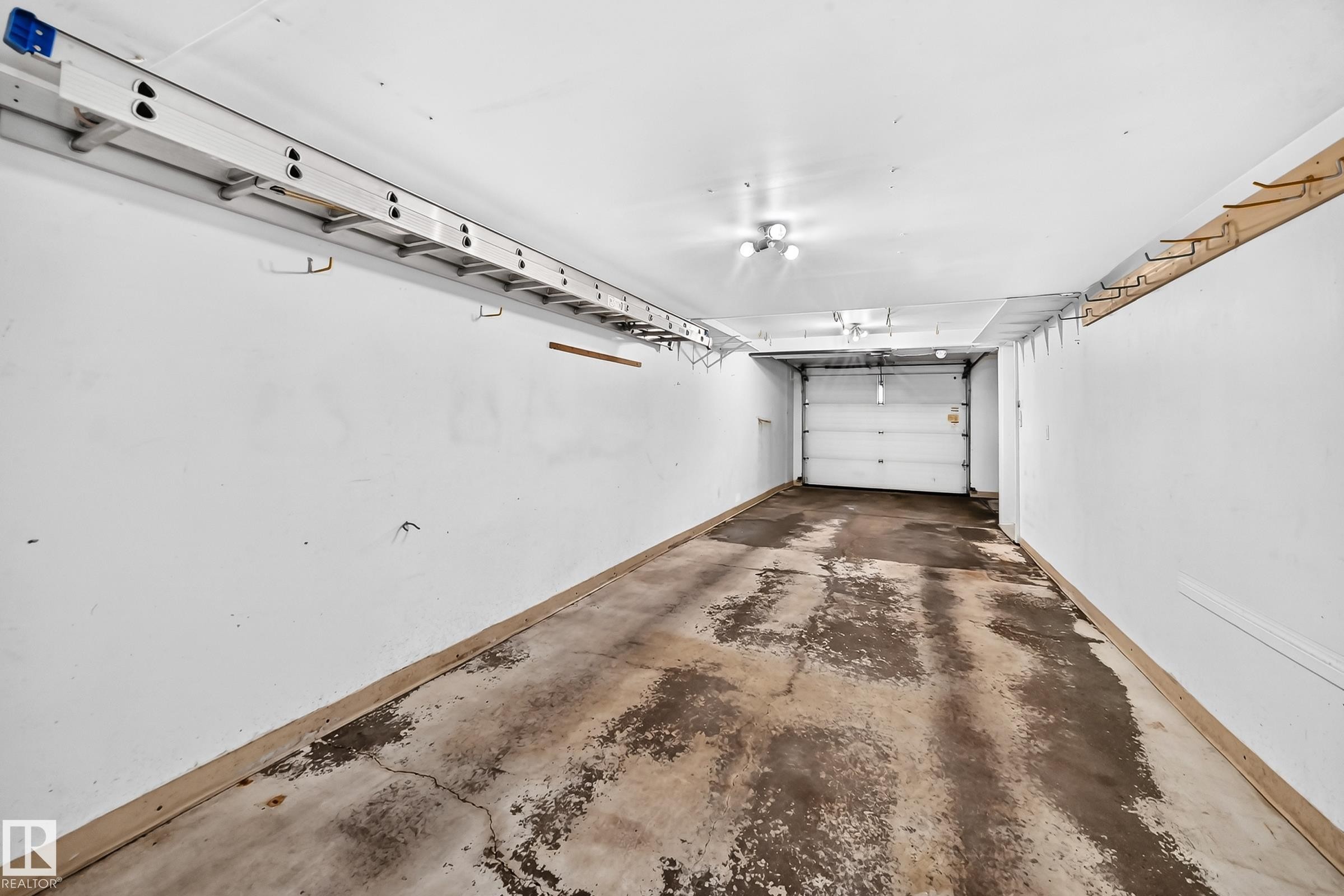 Spacious garage featuring a concrete floor, overhead lighting, and white painted walls - #51 9630 176 St Nw, Edmonton, AB - Indoor Photo Showing Garage