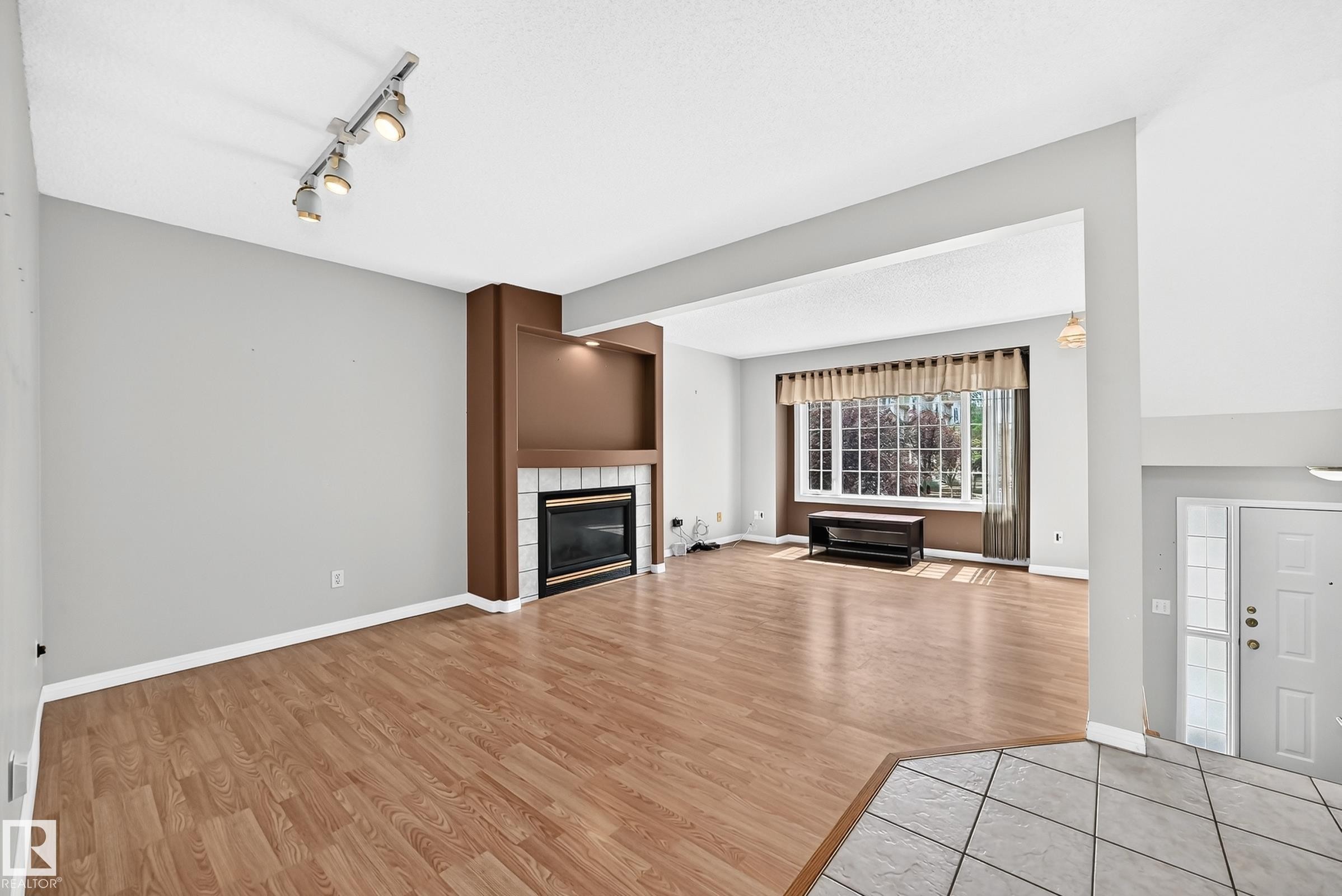 Living area featuring wood-finish flooring and a fireplace with a white tiled surround and built-in shelving - #51 9630 176 St Nw, Edmonton, AB - Indoor Photo Showing Living Room With Fireplace