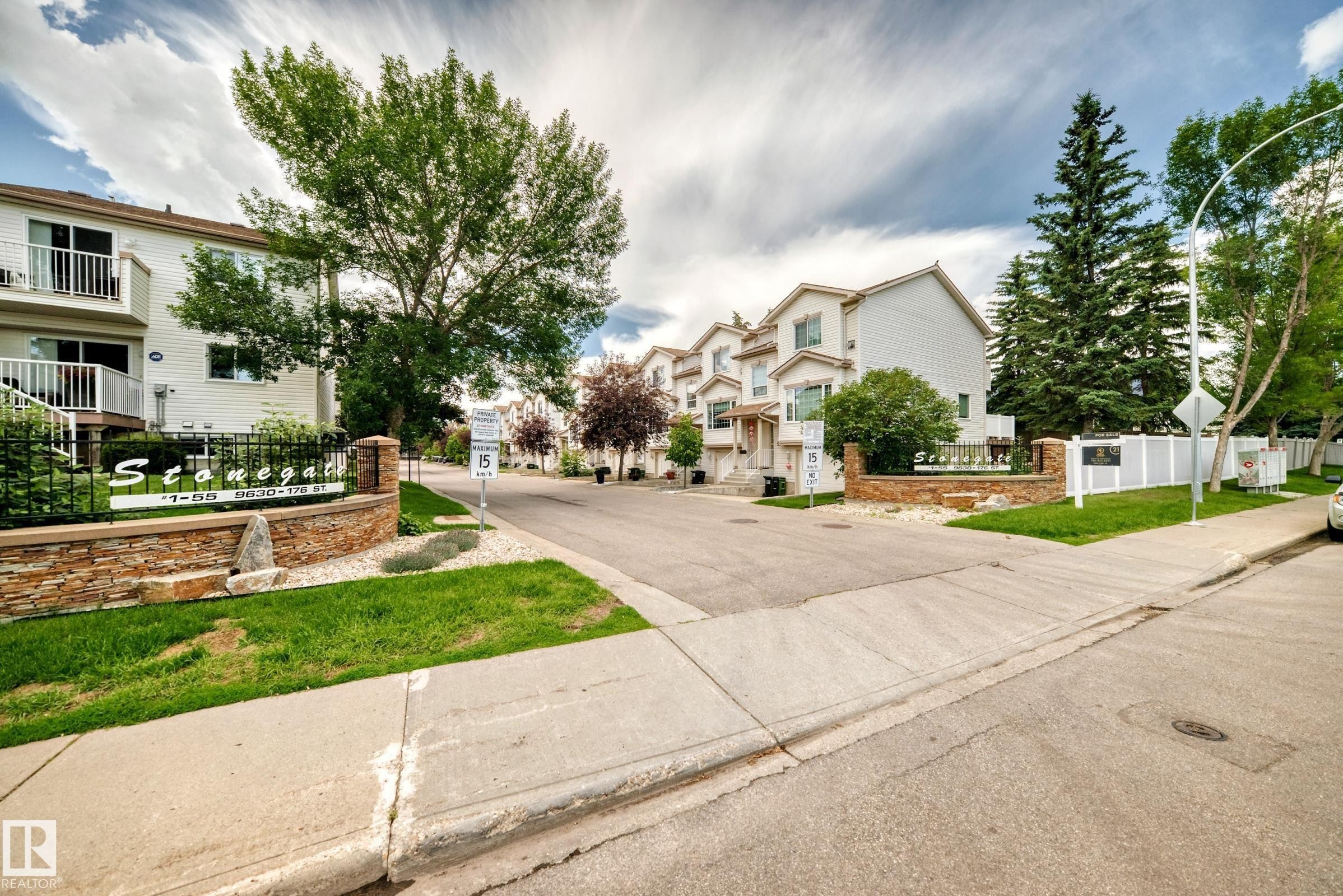 Entryway featuring a stone-clad monument sign, wrought iron accents, and mature landscaping - #51 9630 176 St Nw, Edmonton, AB - Outdoor