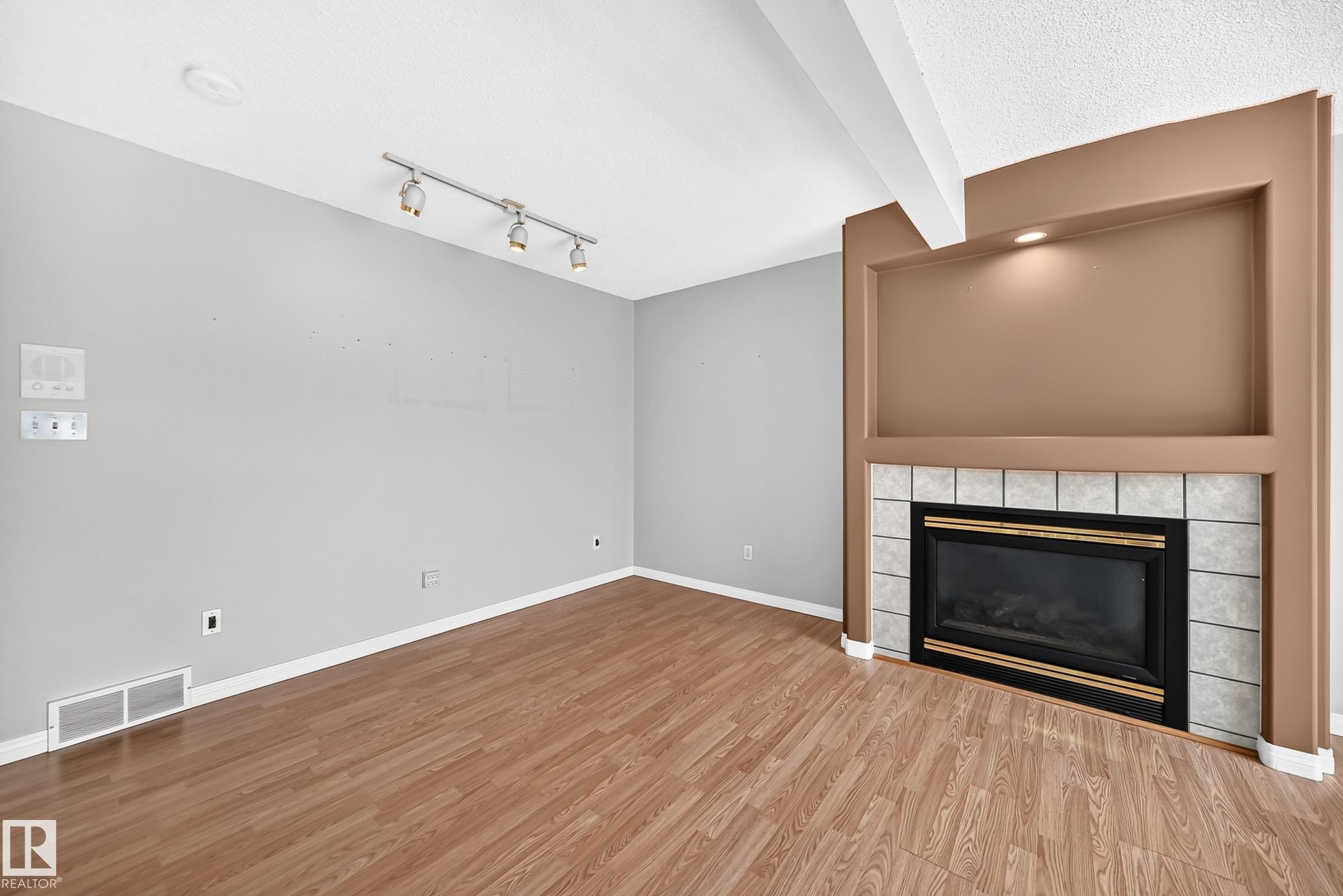 Living area featuring wood-finish flooring and a fireplace with a tiled surround - #51 9630 176 St Nw, Edmonton, AB - Indoor Photo Showing Other Room With Fireplace