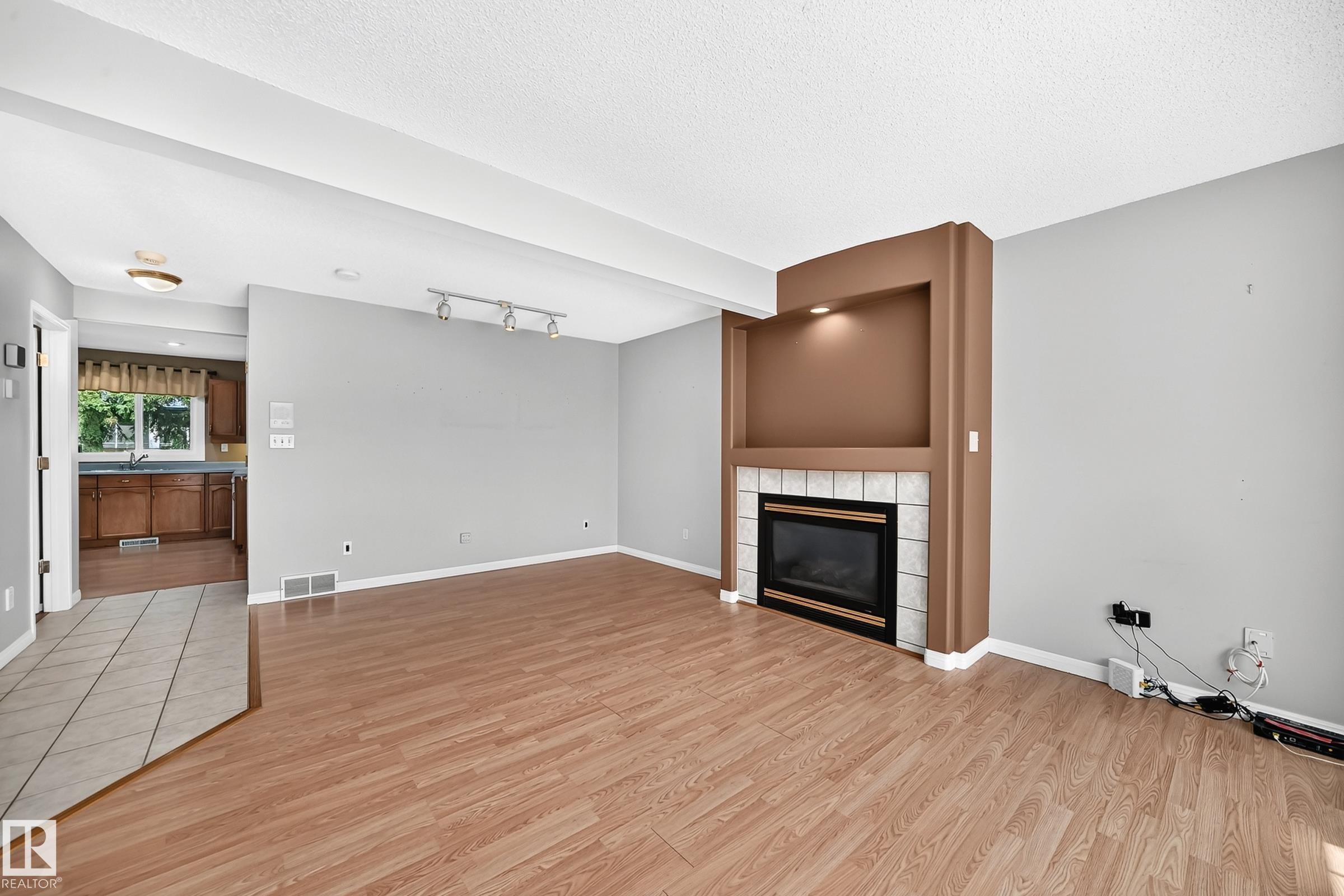 Living area featuring wood-finish flooring, a built-in fireplace with a tiled hearth, an integrated niche with accent lighting, and track lighting - #51 9630 176 St Nw, Edmonton, AB - Indoor With Fireplace