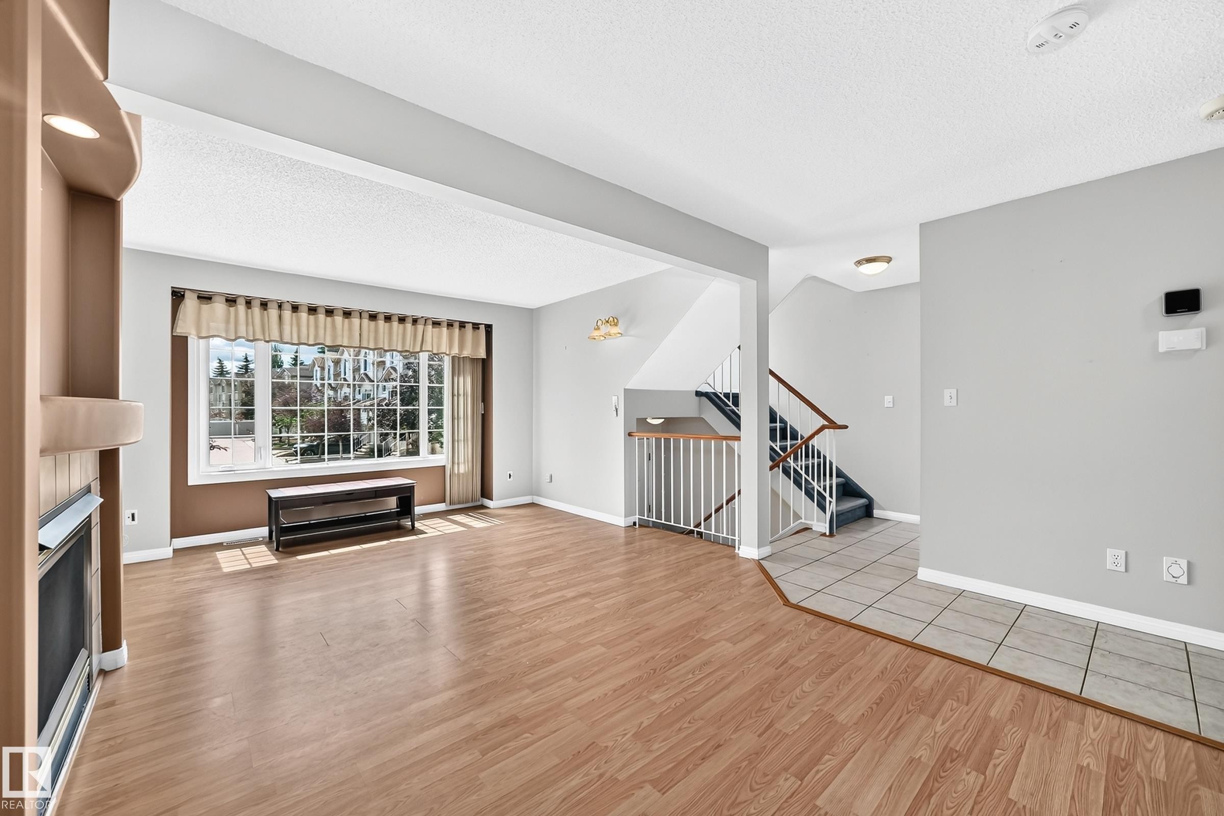 Spacious living area featuring wood-finish flooring, a large multi-pane window, and a built-in fireplace with an integrated niche - #51 9630 176 St Nw, Edmonton, AB - Indoor Photo Showing Living Room