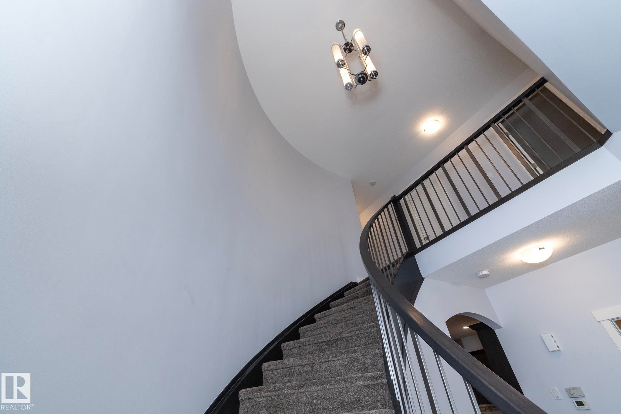 Curved staircase with carpeted treads and dark wood-finish handrail, featuring black metal balusters - 2016 Redtail Common, Edmonton, AB