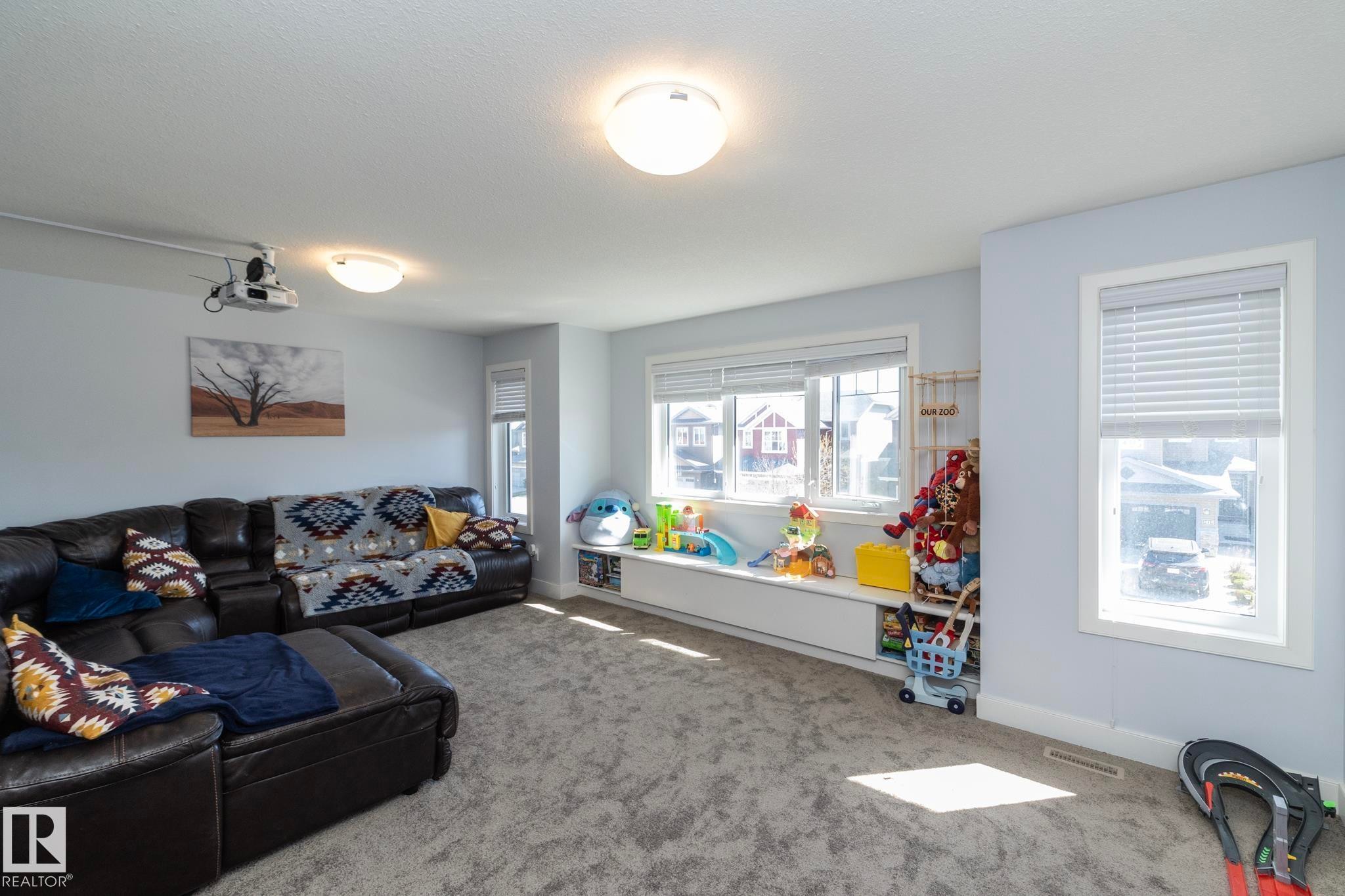 Spacious room featuring light blue walls, gray carpet flooring, and multiple windows with white blinds - 2016 Redtail Common, Edmonton, AB