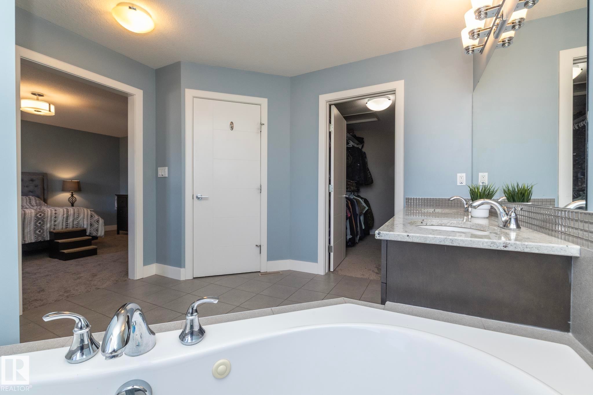 Bathroom featuring a corner soaking tub with chrome fixtures, a single vanity with a light-toned countertop and undermount sink, and tile flooring - 2016 Redtail Common, Edmonton, AB