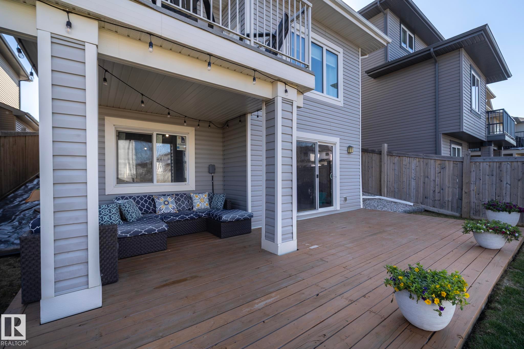 Expansive wood deck with a covered patio area, featuring string lighting, a sliding glass door, and exterior siding - 2016 Redtail Common, Edmonton, AB