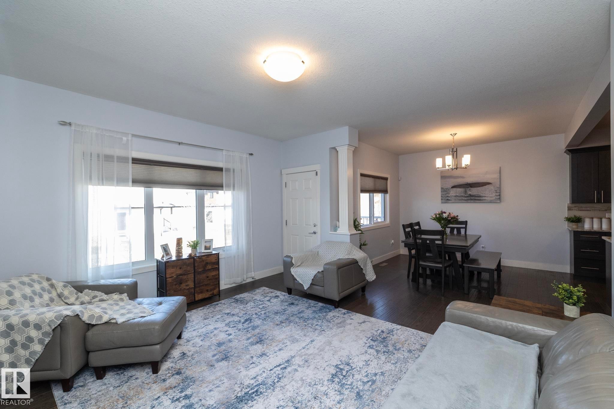 Open-concept living space featuring dark wood-finish flooring, recessed lighting, and a dining area with a four-light chandelier - 2016 Redtail Common, Edmonton, AB