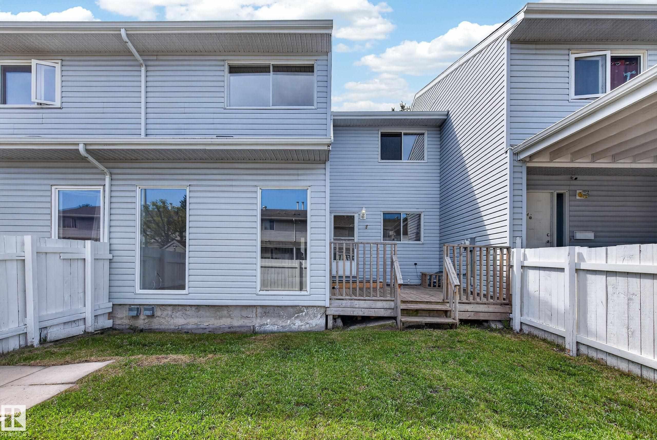 Rear exterior featuring light blue vinyl siding, multiple windows, a wooden deck, and a fenced yard with grass and a concrete path - 156 Lee Ridge Road, Edmonton, AB - Outdoor With Exterior