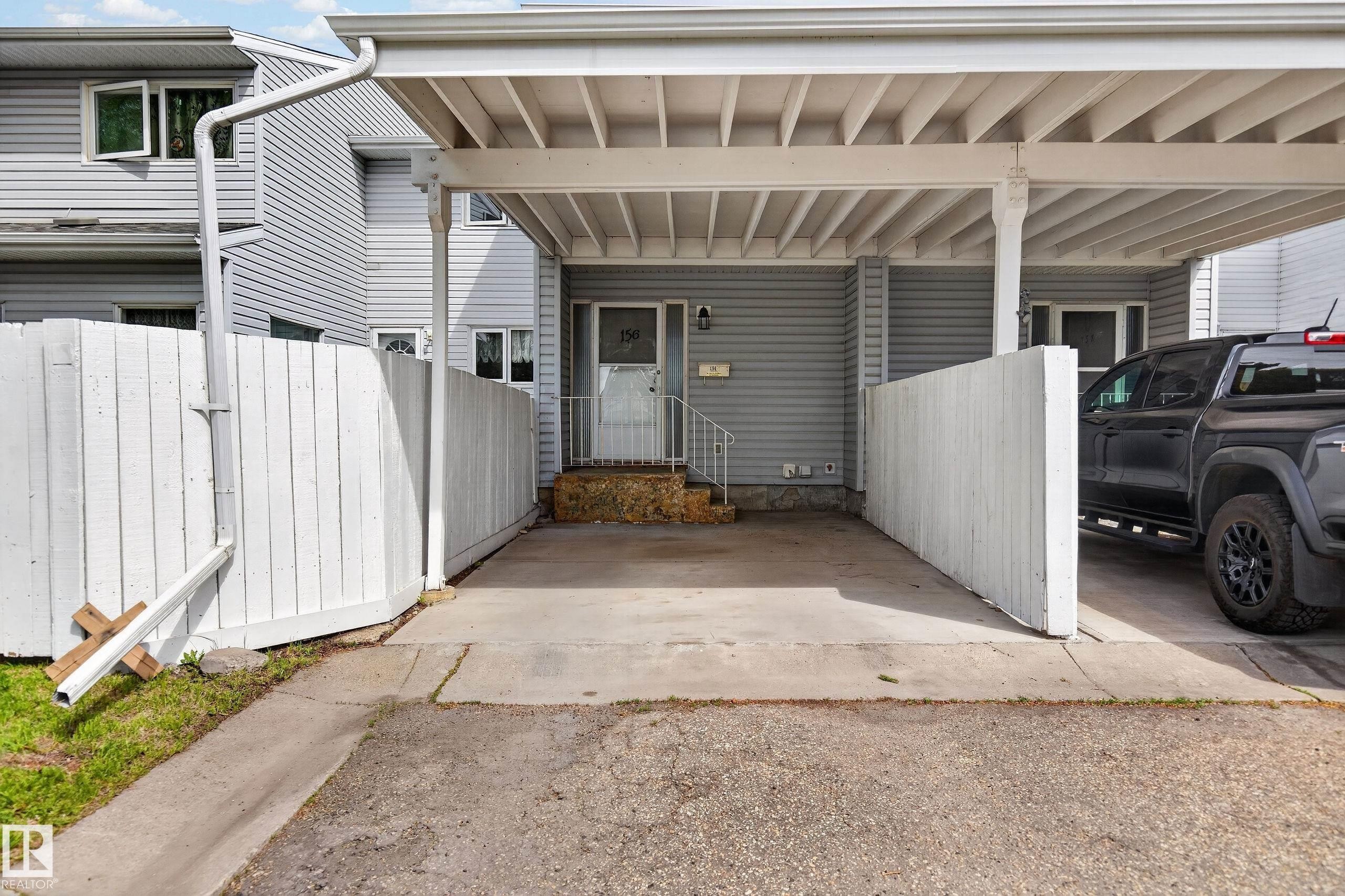 Covered carport providing sheltered parking, gray horizontal siding exterior, white picket fencing, and an inviting entry with steps - 156 Lee Ridge Road, Edmonton, AB - Outdoor With Exterior