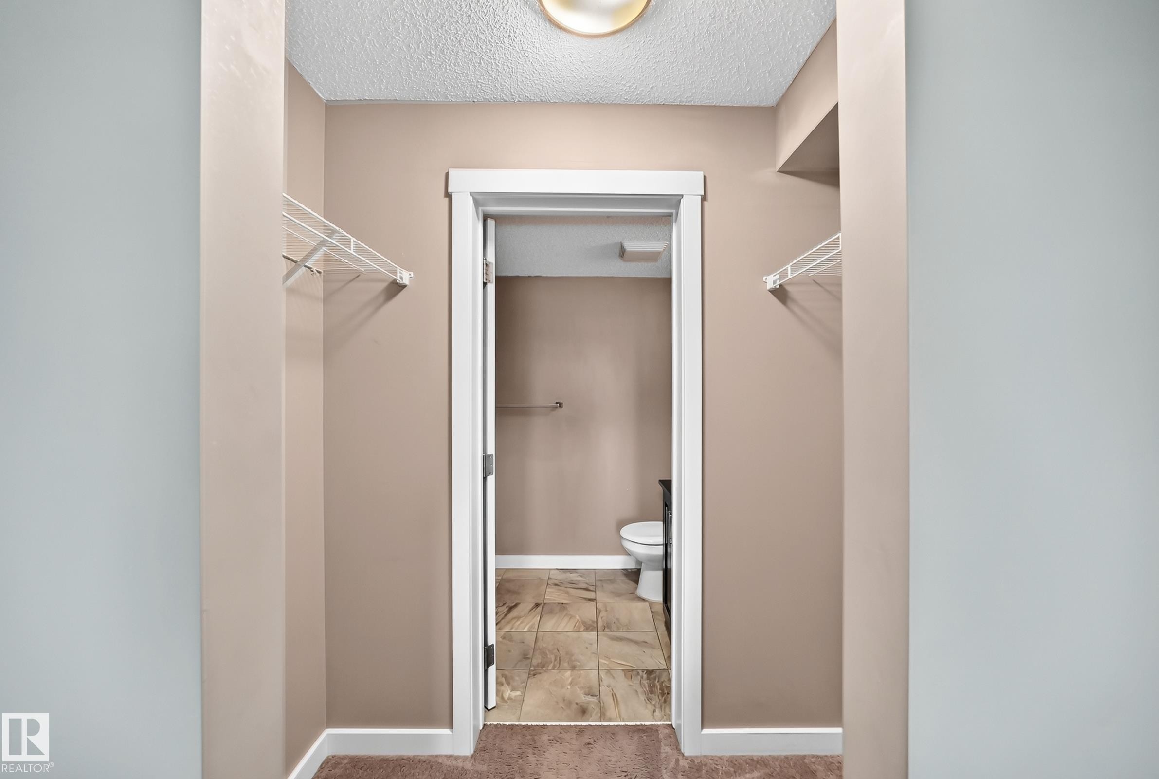 Hallway with built-in wire shelving and a doorway leading to a room with tiled flooring and a toilet - 308 18126 77 Street, Edmonton, AB