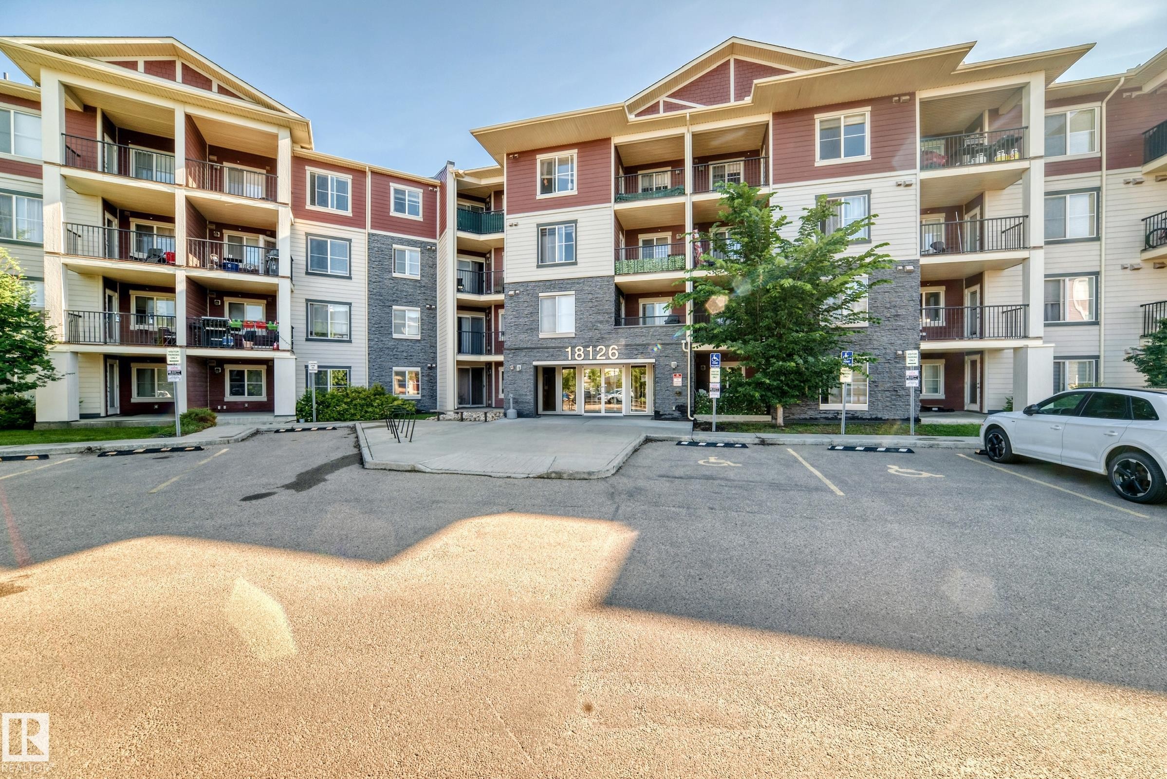 Multi-story residential building featuring a stone and siding exterior, multiple private balconies with black railings, and a prominent main entrance - 308 18126 77 Street, Edmonton, AB