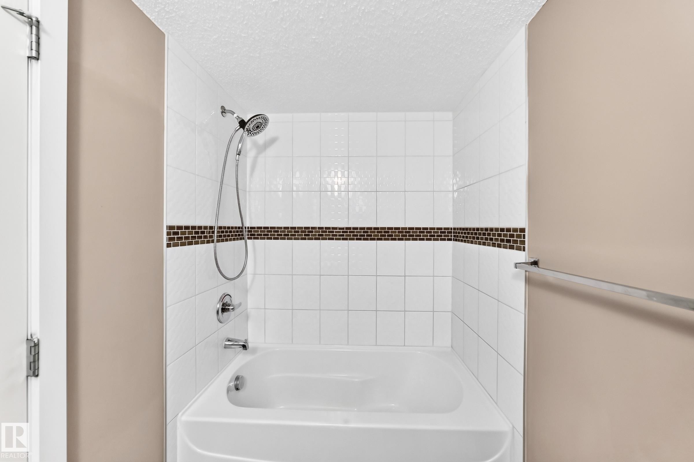 Bathtub and shower combination featuring white subway tile, a decorative mosaic tile accent band, and chrome fixtures - 308 18126 77 Street, Edmonton, AB