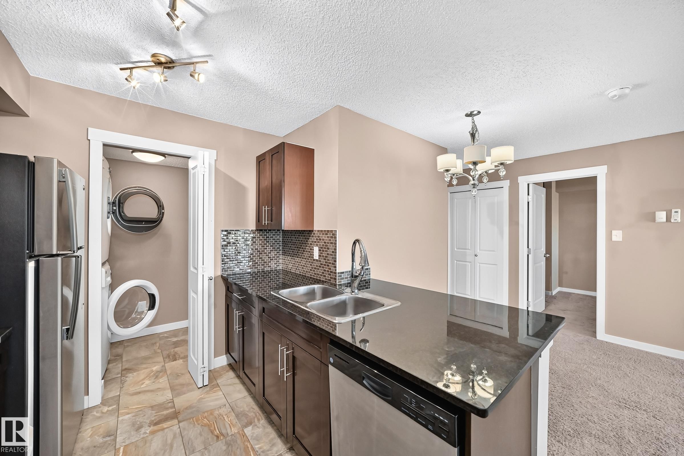 Kitchen island with dark countertop, stainless steel double basin sink, and integrated dishwasher - 308 18126 77 Street, Edmonton, AB