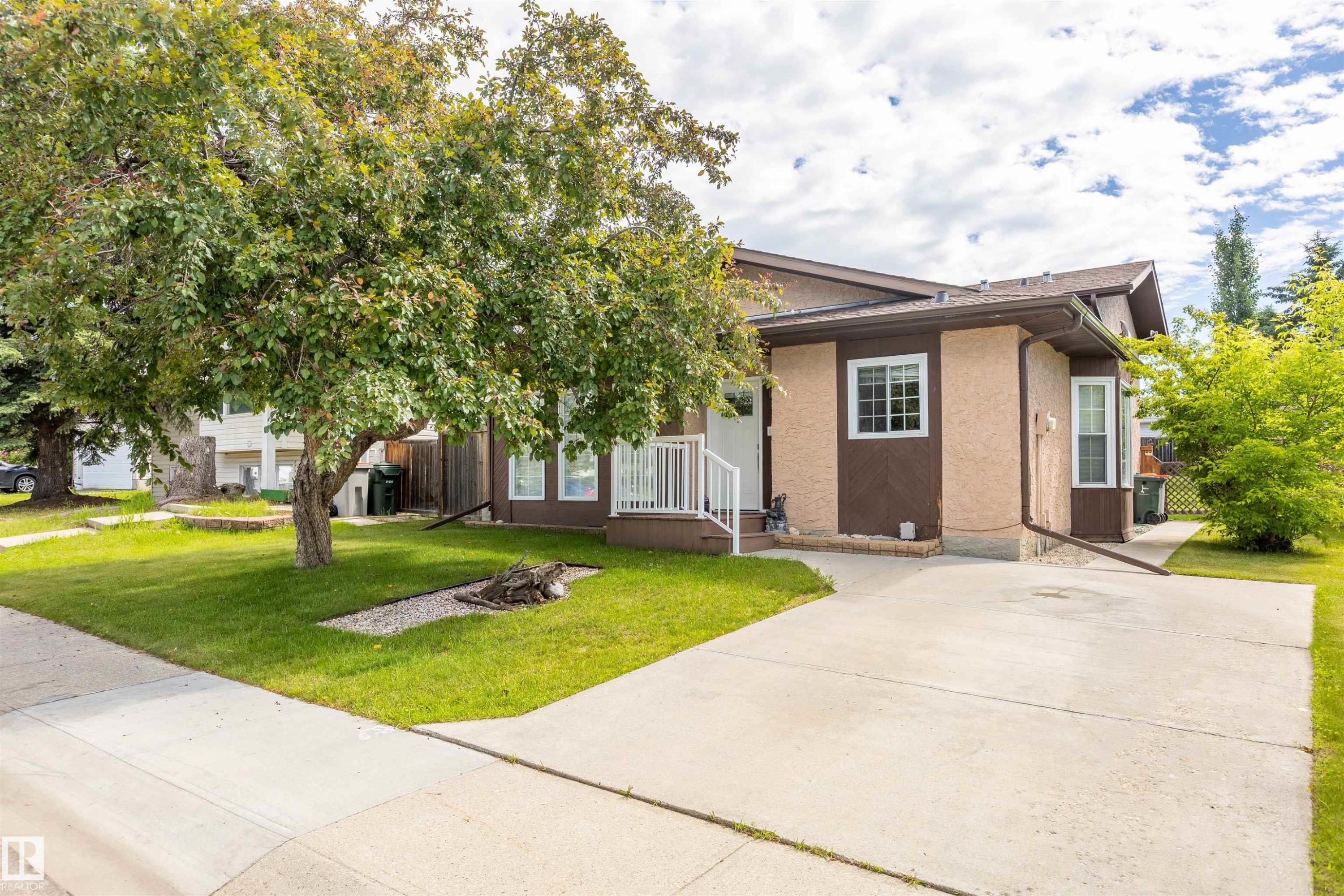 Contemporary exterior featuring two-tone stucco siding, white window frames, an angled roofline, and a concrete driveway - 3 Glenforest Crescent, Stony Plain, AB