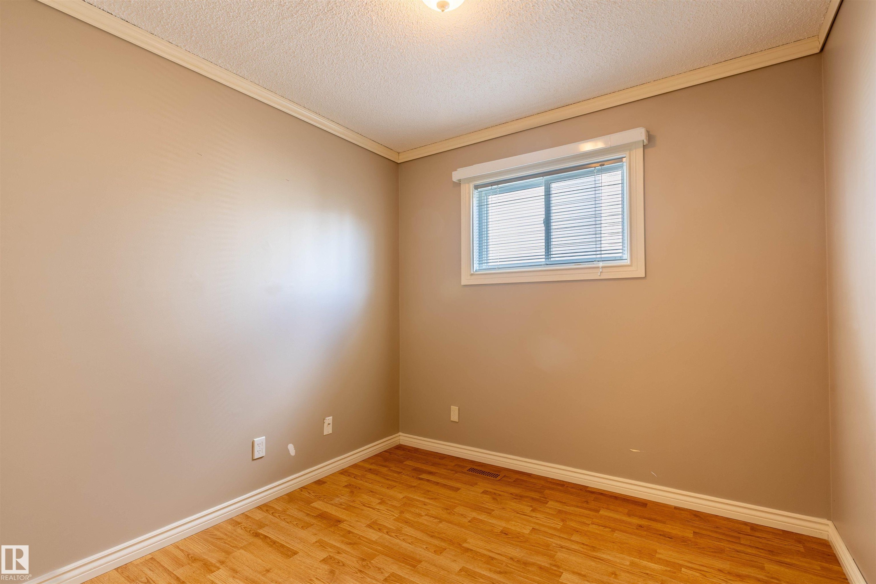 Bedroom featuring light beige walls, wood-finish flooring, white baseboards, and crown molding - 3 Glenforest Crescent, Stony Plain, AB