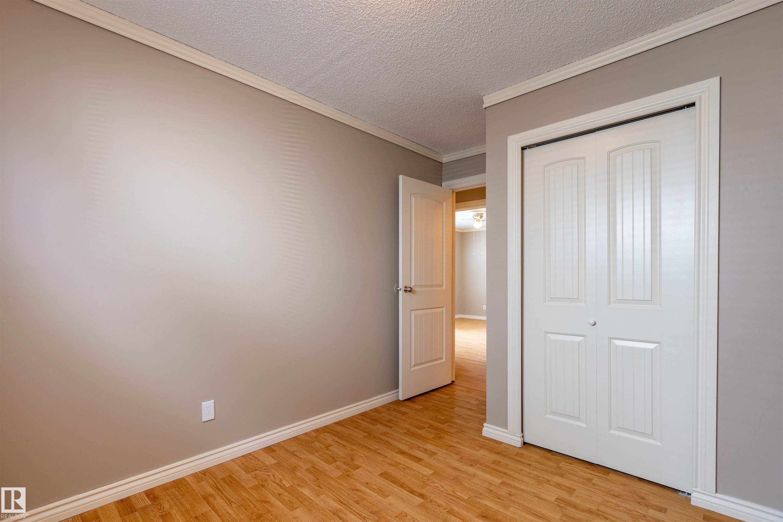 Room featuring wood-finish flooring, neutral wall paint, white baseboards, and crown molding - 3 Glenforest Crescent, Stony Plain, AB