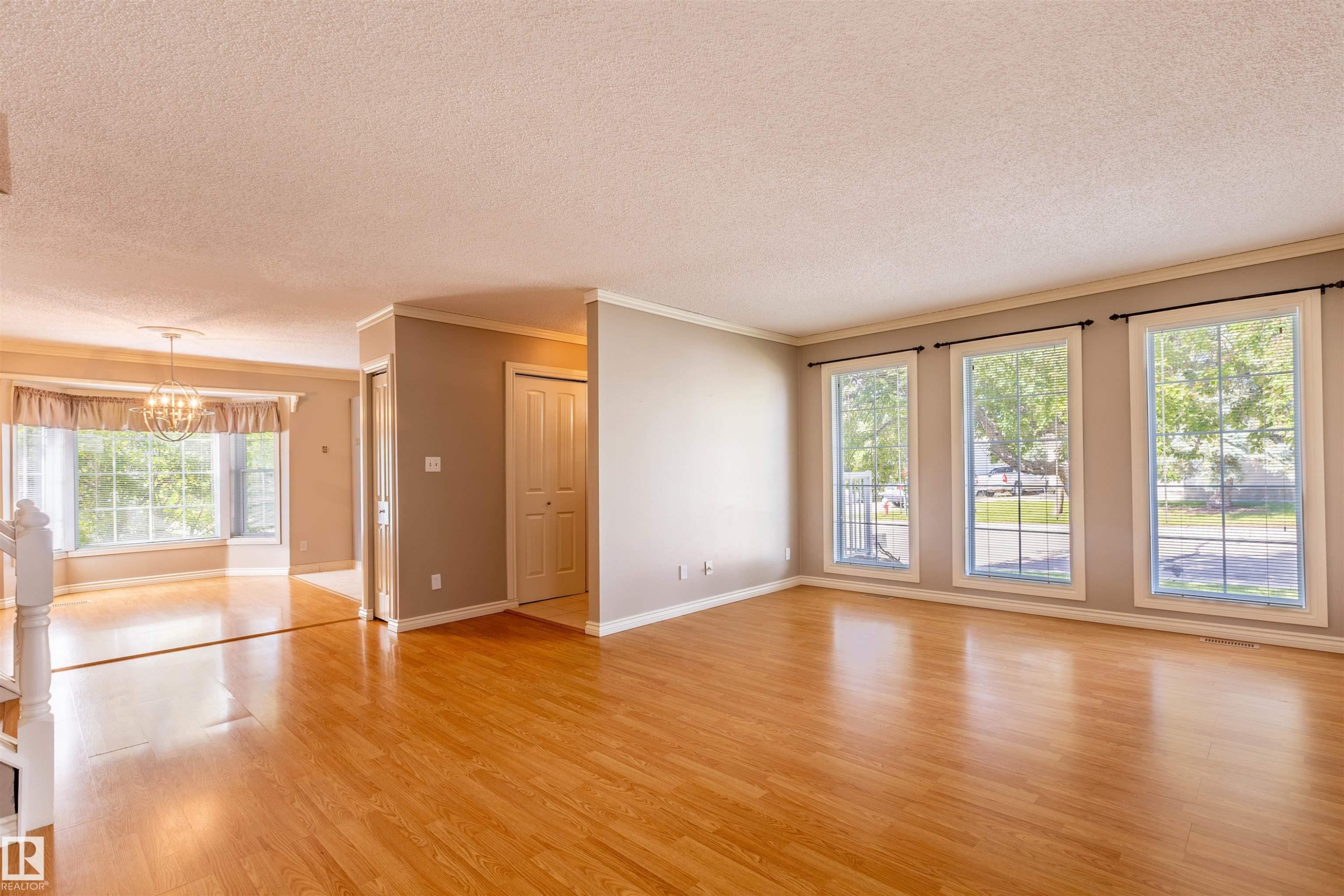 Spacious interior featuring wood-finish flooring throughout, multiple large windows providing abundant illumination, crown molding, and a visible chandelier in the dining area - 3 Glenforest Crescent, Stony Plain, AB