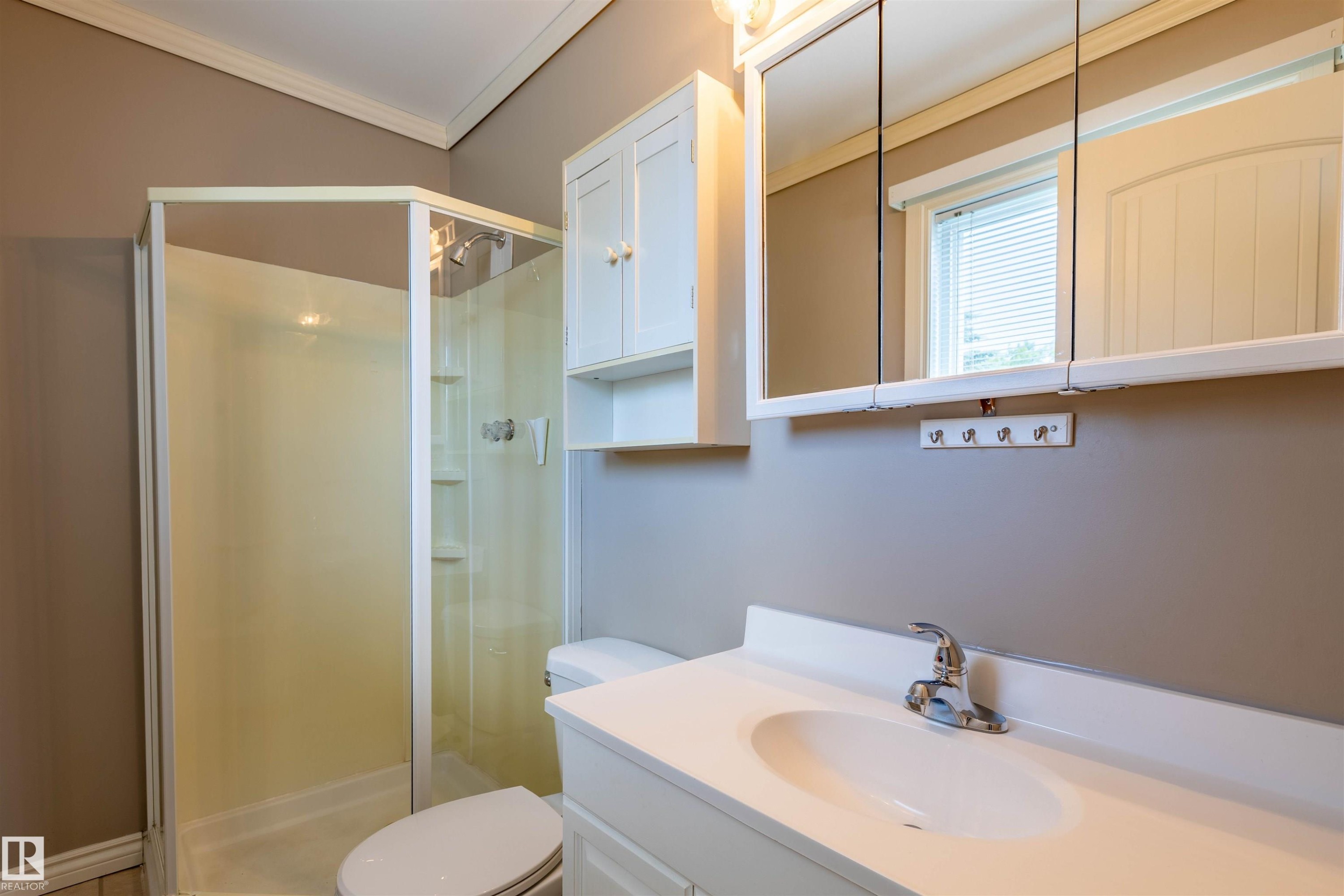 Bathroom featuring a corner shower with glass enclosure, white vanity with integrated sink, chrome faucet, and mirrored medicine cabinet - 3 Glenforest Crescent, Stony Plain, AB