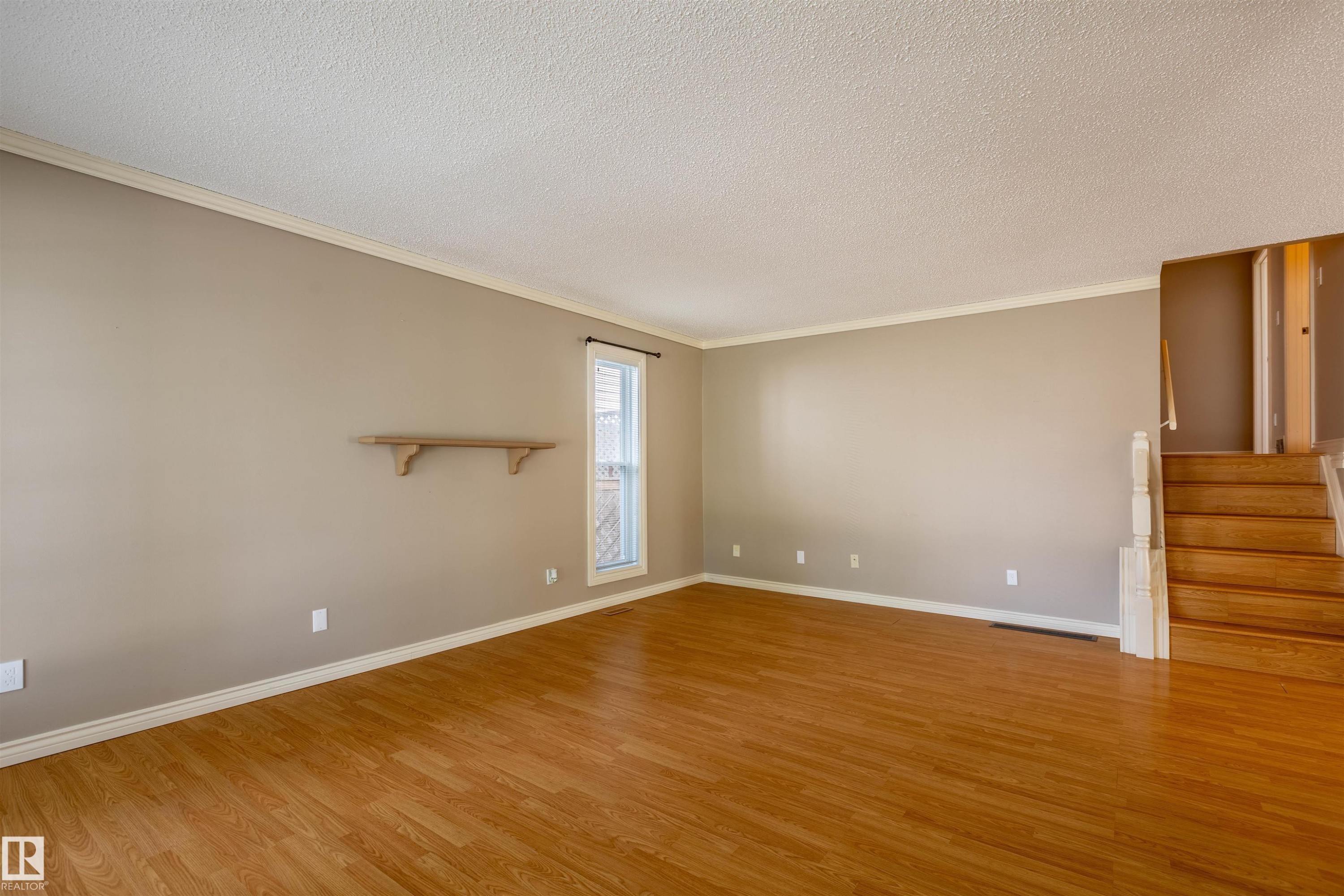 Spacious room featuring wood-finish flooring, neutral-toned walls, and white crown molding - 3 Glenforest Crescent, Stony Plain, AB