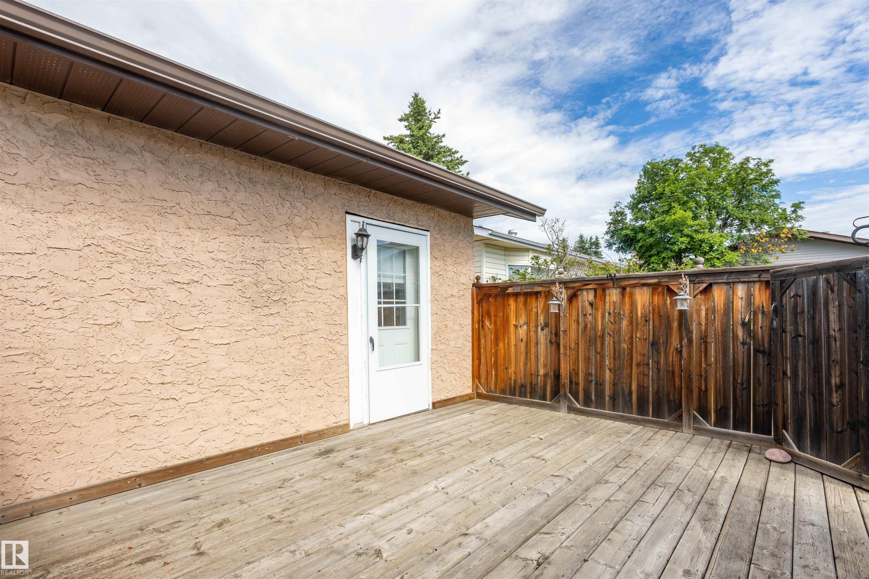 Private outdoor deck area featuring wood decking, a full-lite exterior door, stucco siding, and a wood privacy fence - 3 Glenforest Crescent, Stony Plain, AB