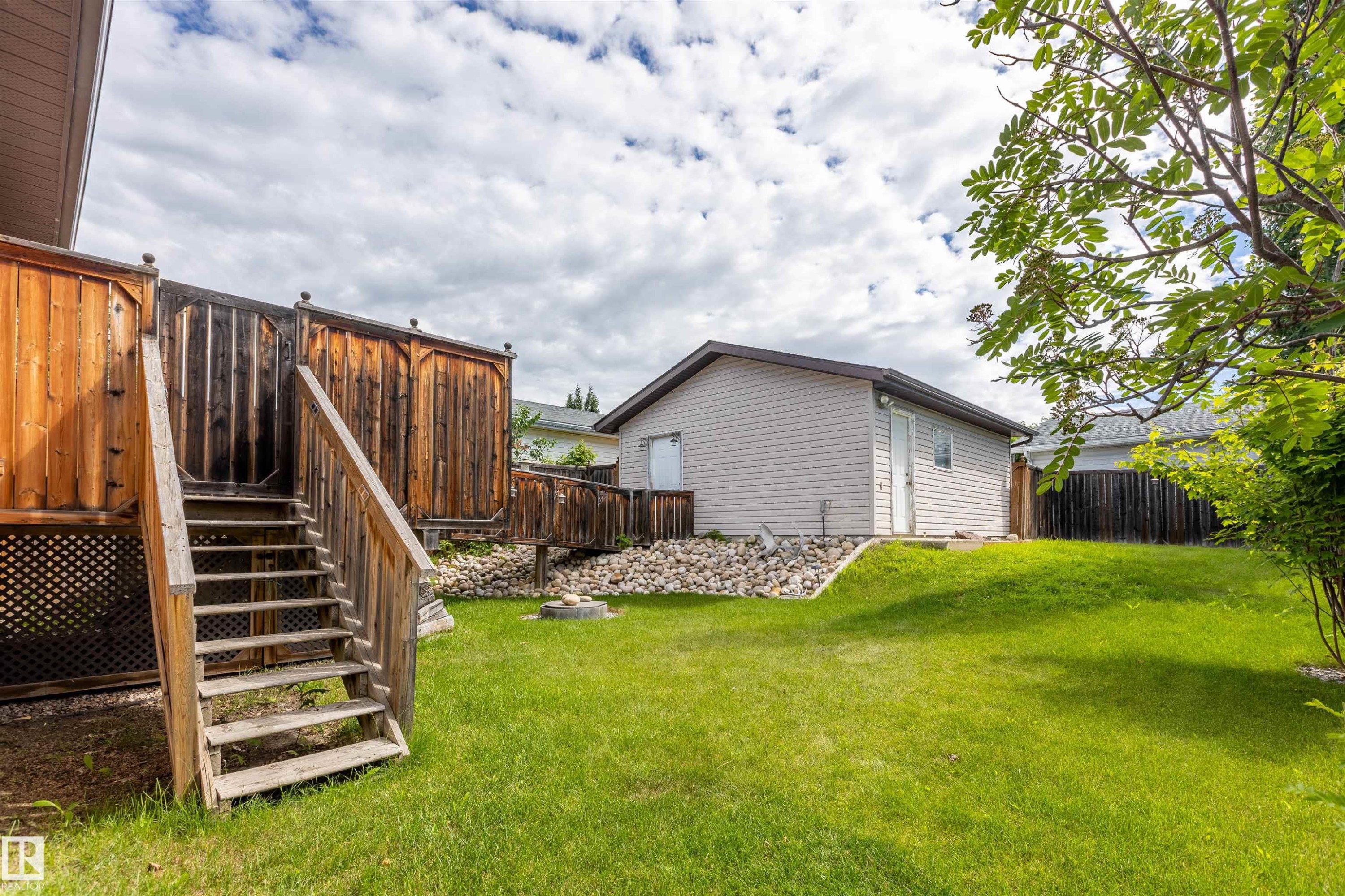 Wooden deck with privacy screening, stairs, and lattice skirting overlooking a grass lawn - 3 Glenforest Crescent, Stony Plain, AB