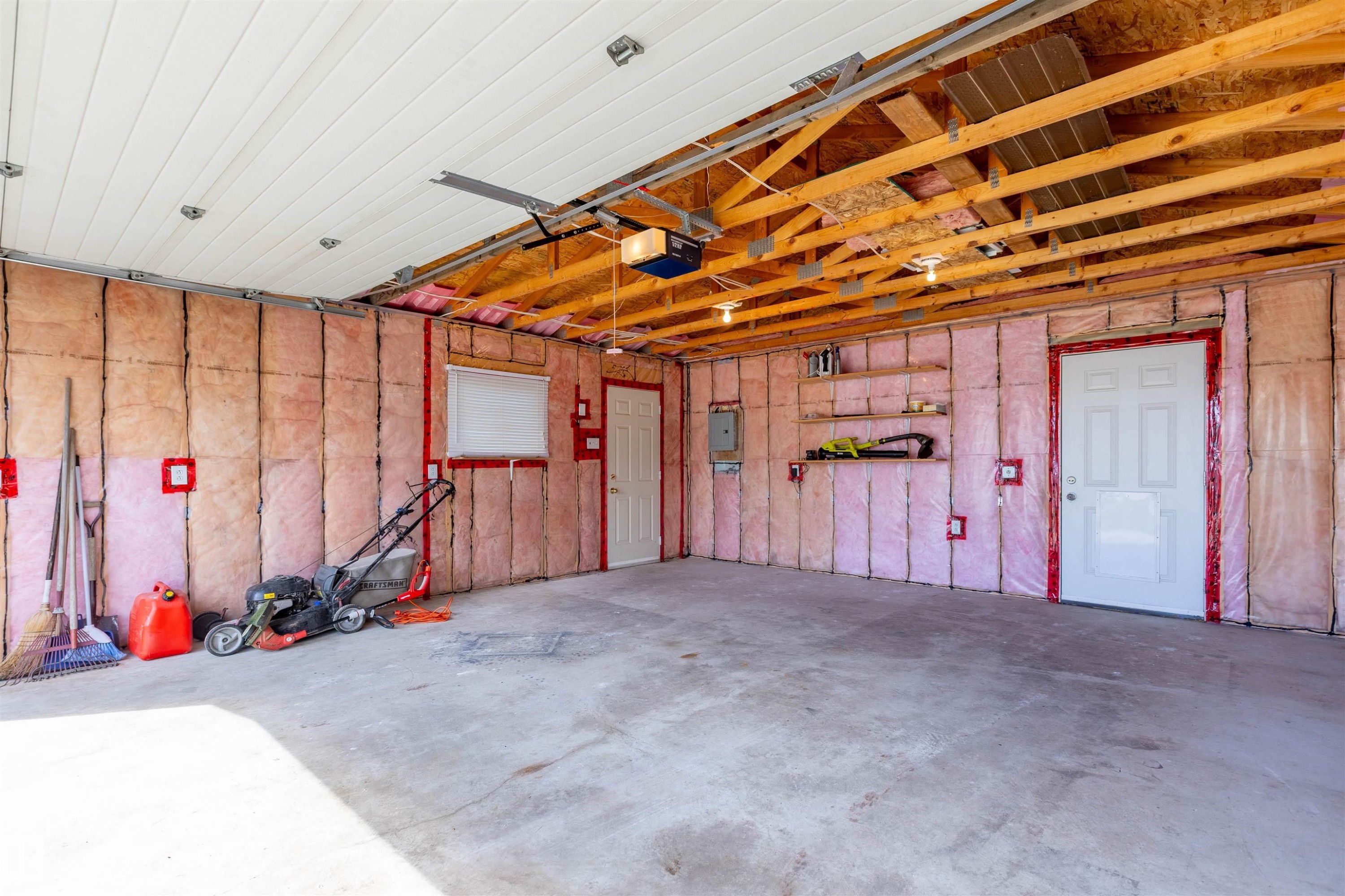 Spacious garage featuring exposed wood ceiling trusses, insulated walls, concrete flooring, and multiple entry points - 3 Glenforest Crescent, Stony Plain, AB