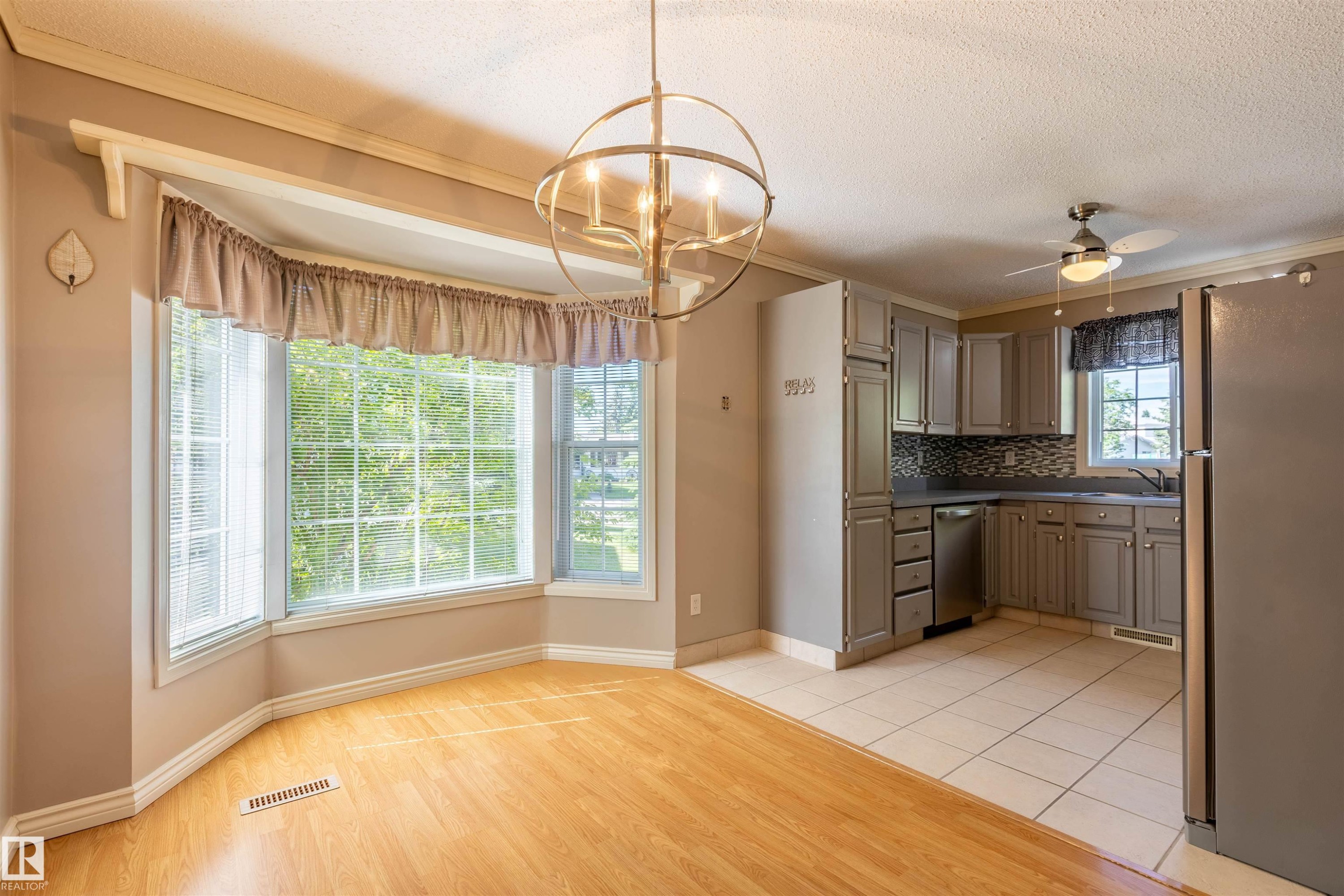 Integrated kitchen and dining area featuring a bay window, wood-finish flooring, tile flooring, updated cabinetry, and a ceiling fan - 3 Glenforest Crescent, Stony Plain, AB