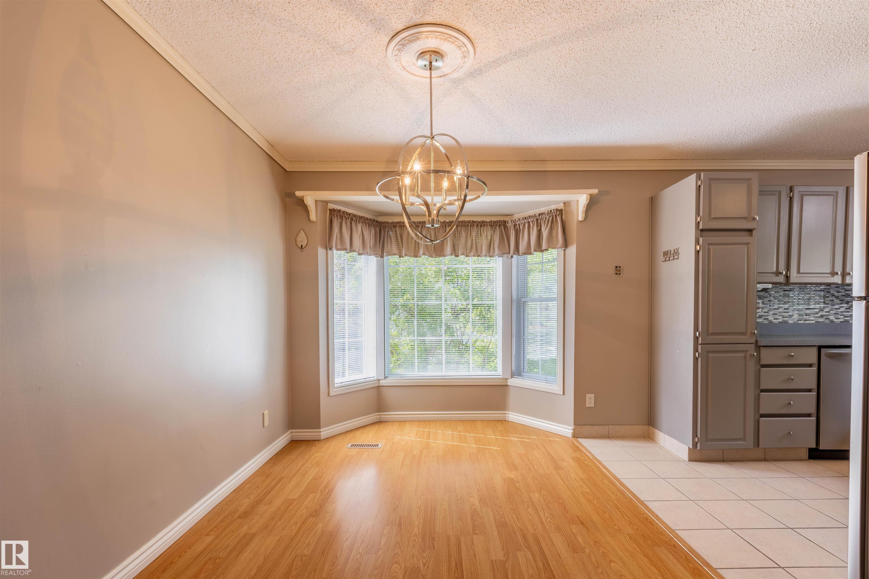 Bright dining area featuring a bay window, wood-finish flooring, and a contemporary chandelier - 3 Glenforest Crescent, Stony Plain, AB