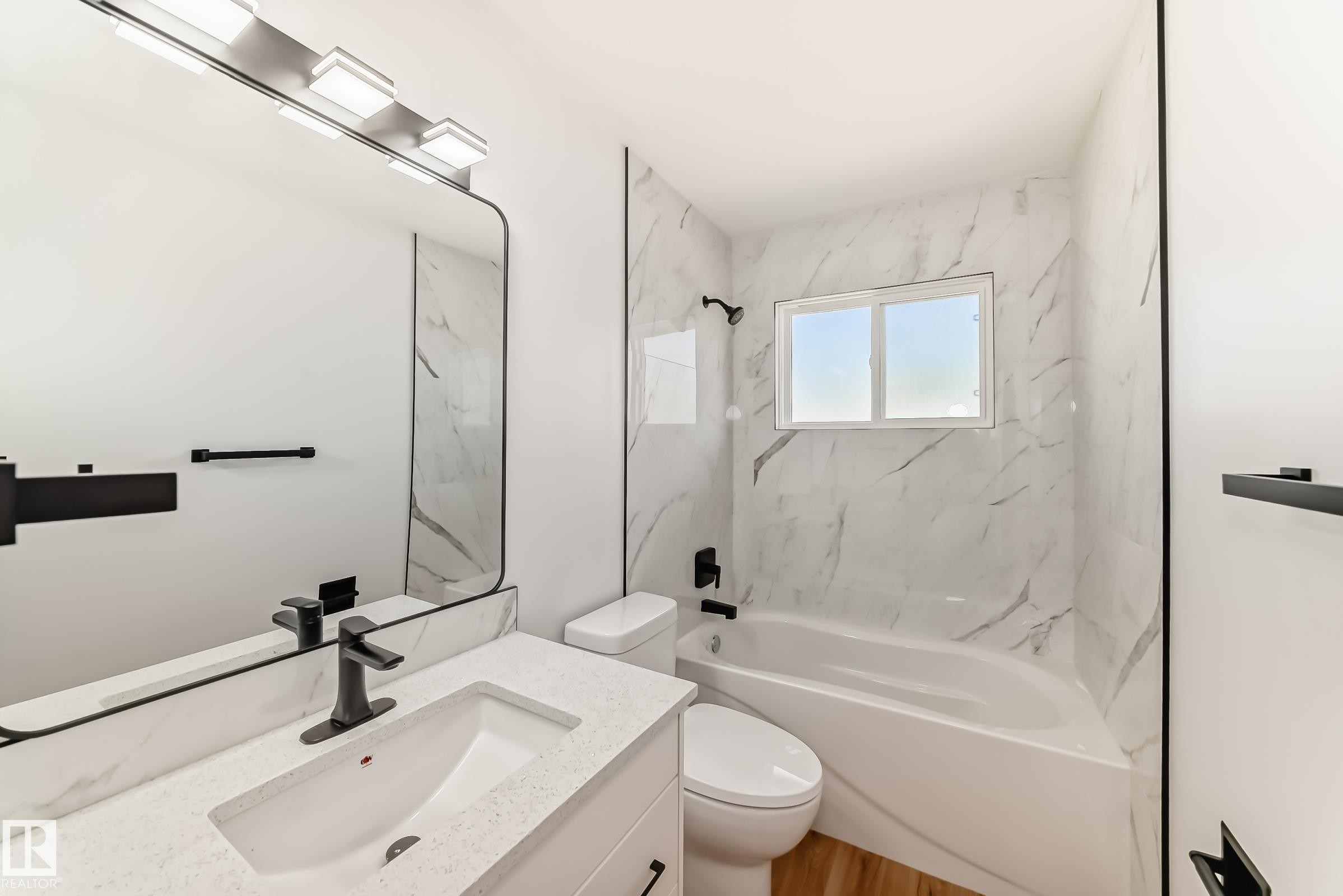 Bathroom featuring a white vanity with an integrated sink, a solid surface countertop, and a large mirror with a black frame - 4842 116Ave, Edmonton, AB