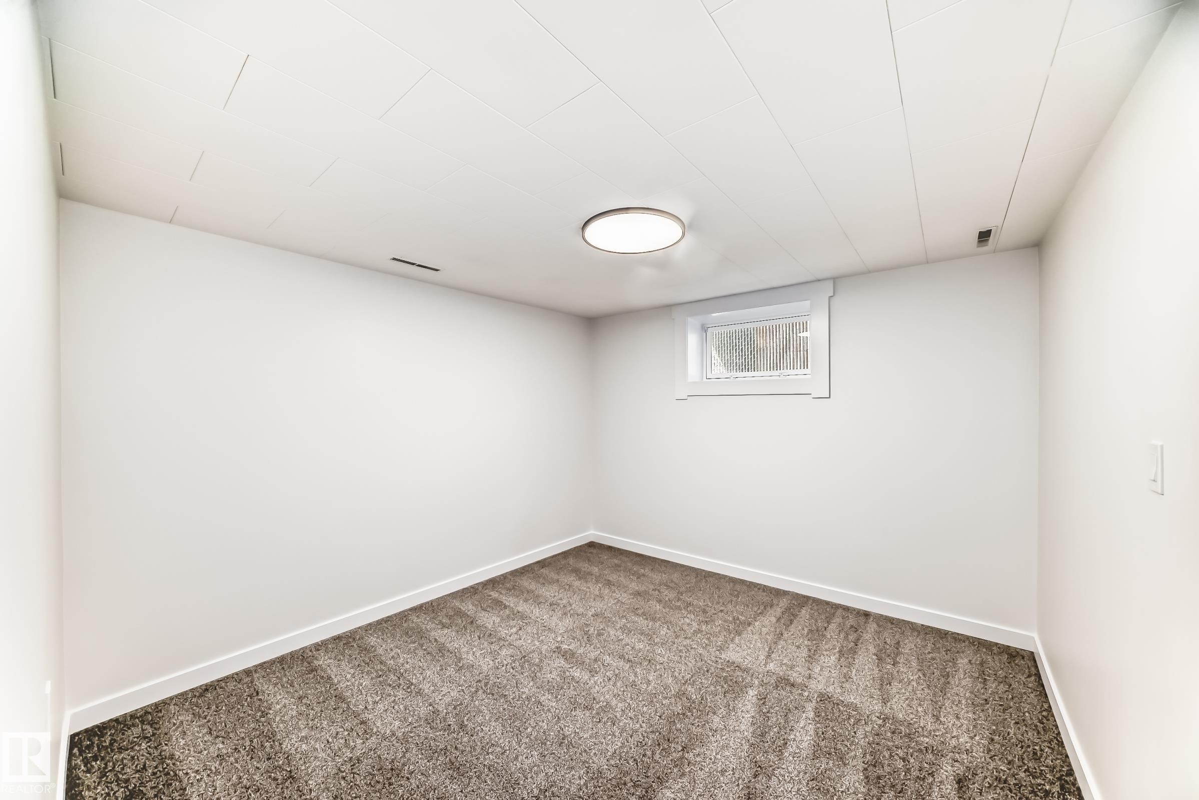 Carpeted room featuring white walls, a single window with white trim, a flush-mount ceiling light fixture, and a white paneled ceiling - 4842 116Ave, Edmonton, AB