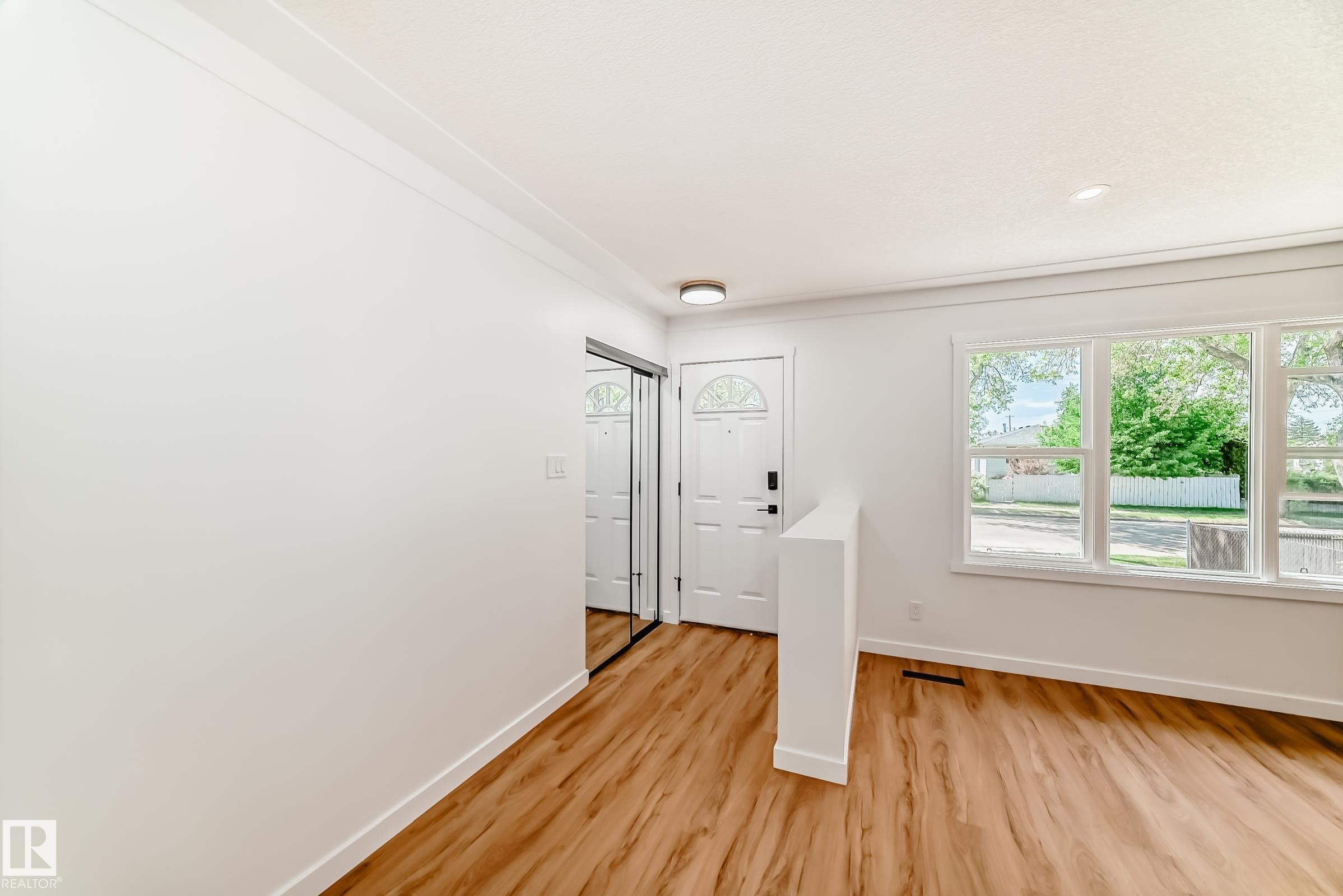 Bright entryway featuring wood-finish flooring, a white front door with decorative glass, and a mirrored sliding closet door - 4842 116Ave, Edmonton, AB
