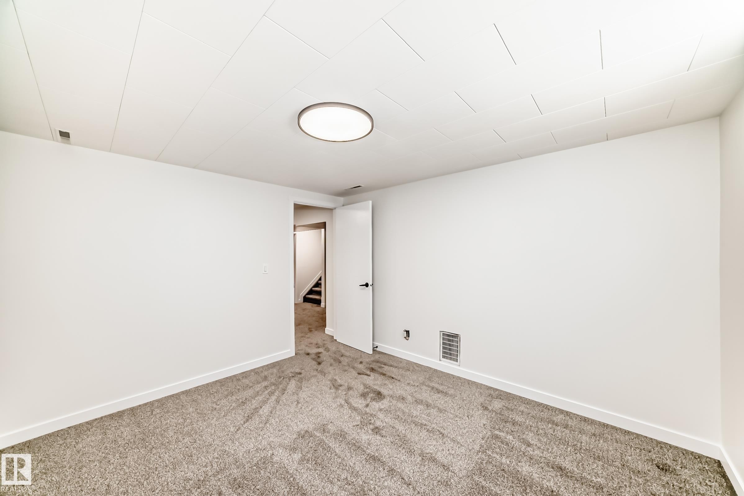 Carpeted room featuring white walls, white trim, and a white ceiling with an integrated flush-mount circular light fixture - 4842 116Ave, Edmonton, AB